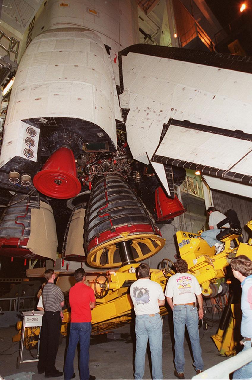 KENNEDY SPACE CENTER, FLA. -- Workers in the Vehicle Assembly Building watch as Space Shuttle Atlantis' Main Engine No. 1 is being removed. An inventory review concerning defective main engine fuel pump tip seals indicated that defective seals may be present on the fuel pump for the engine. The decision was made to replace the suspect engine with one originally slated for Discovery. The main engine nozzle, visible in the photo, is 7.8 feet across and 9.4 feet high. Space Shuttle Atlantis is scheduled to launch no earlier than April 17, 2000, on mission STS-101 to resupply the International Space Station for the arrival of the next pressurized module, the Russian-built Zvezda