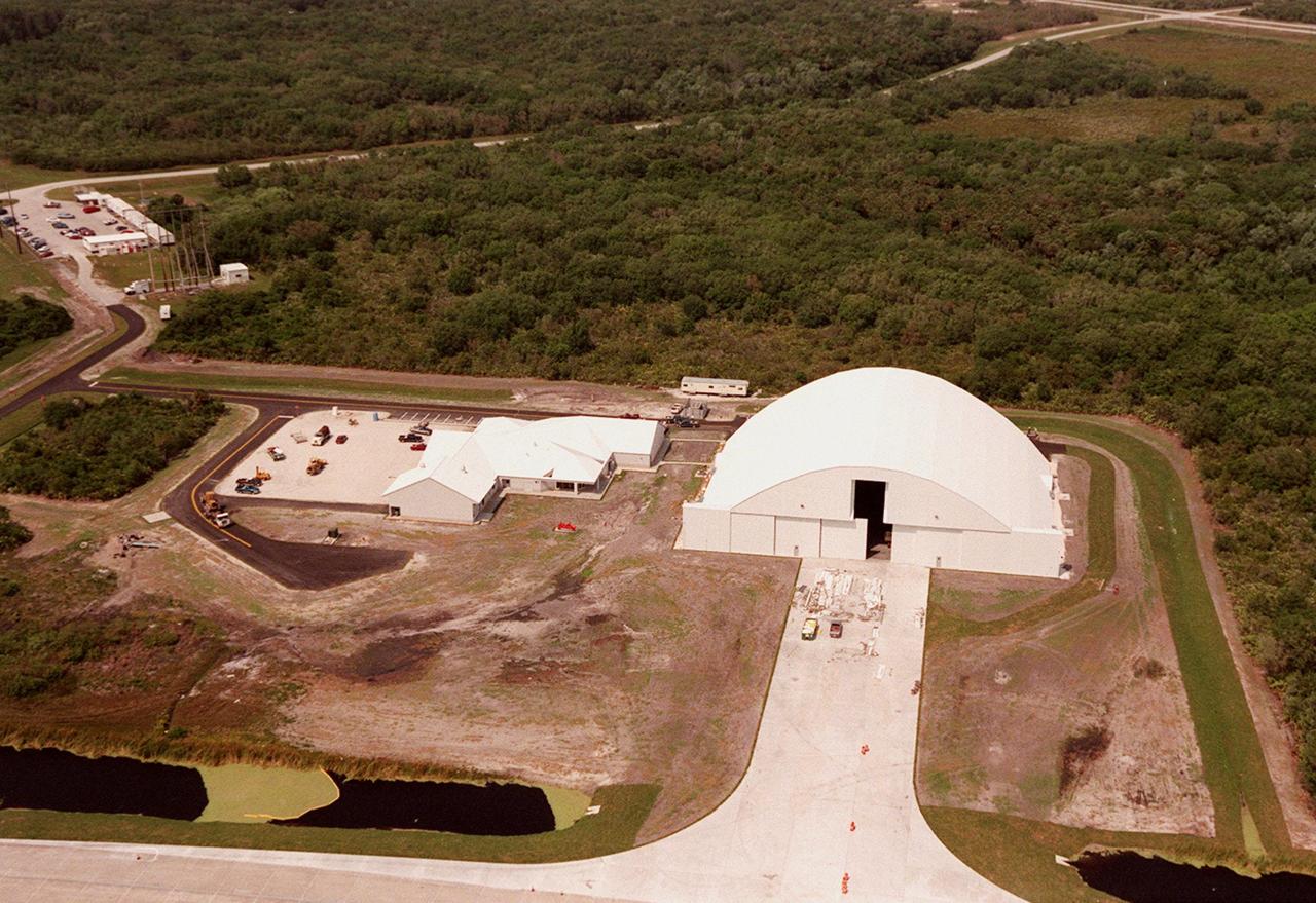 Construction of the new remote launch vehicle hangar (right) is closer to completion. It is at the south end of the Shuttle Landing Facility at KSC. Next to the multi-purpose RLV hangar are facilities for related ground support equipment and administrative/technical support. Astronaut Road is seen near the top of the photo