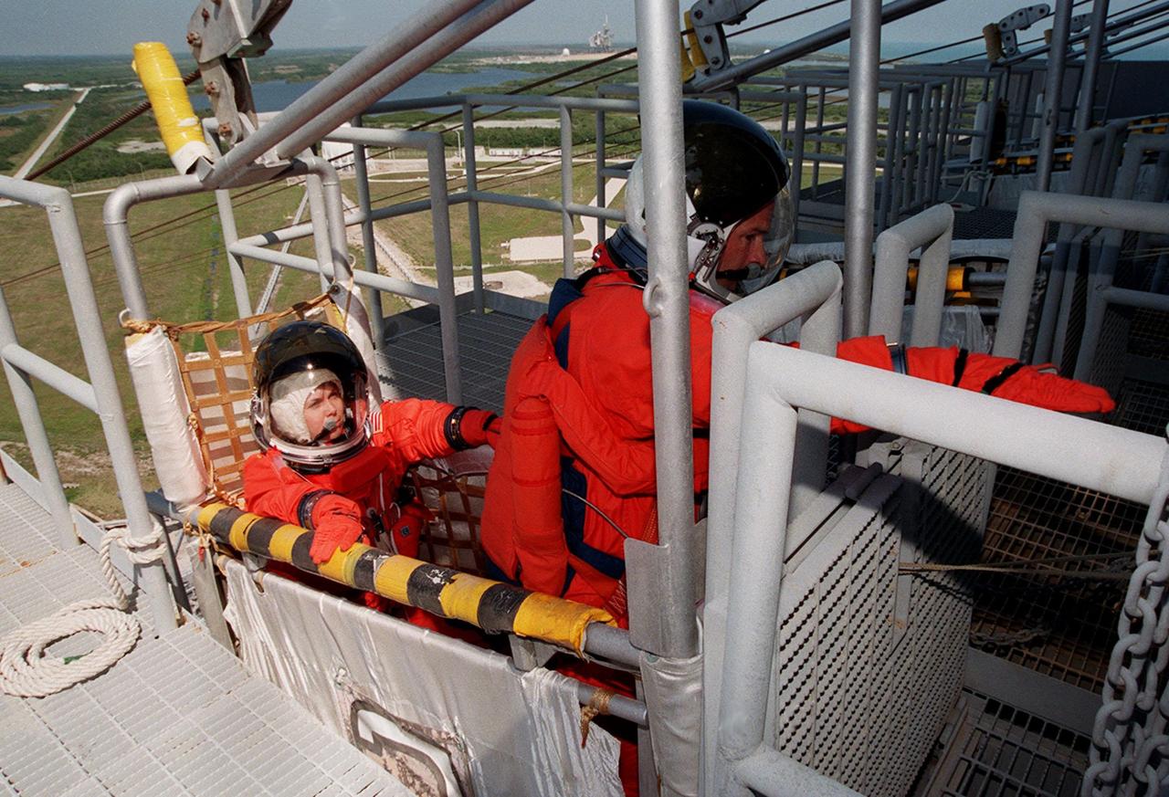 KENNEDY SPACE CENTER, FLA. -- Seated in a slidewire basket at the 195-foot level of the Fixed Service Structure, Launch Pad 39A, are (left to right) STS-101 Mission Specialists Mary Ellen Weber and Jeffrey N. Williams, who is reaching for the release lever. The release of the basket will send it shooting down the 1,200-foot slidewire to a bunker west of the launch pad. The crew is practicing emergency egress from the orbiter as part of Terminal Countdown Demonstration (TCDT) activities that include a simulated launch countdown and familiarization with the payload. During their mission to the International Space Station, the STS-101 crew will be delivering logistics and supplies, plus preparing the Station for the arrival of the Zvezda Service Module, expected to be launched by Russia in July 2000. Also, the crew will conduct one space walk to perform maintenance on the Space Station. This will be the third assembly flight to the Space Station. STS-101 is scheduled to launch April 24 at 4:15 p.m. from Launch Pad 39A