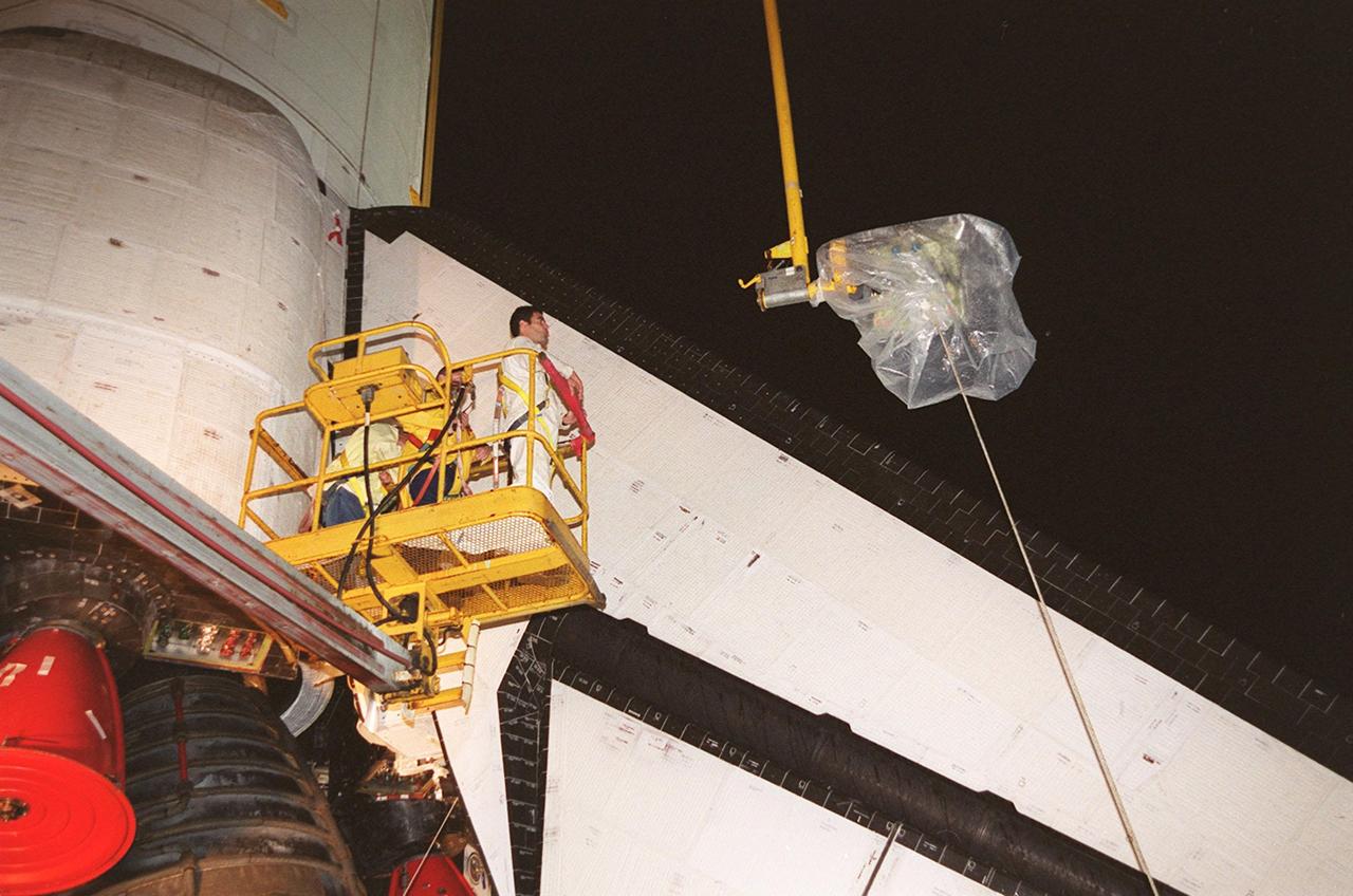 KENNEDY SPACE CENTER, FLA. -- At Launch Pad 39A, a worker watches as the plastic-covered replacement Power Drive Unit (PDU) for Space Shuttle Atlantis is lifted by crane toward the tail. The PDU controls the rudder/speed brake on the orbiter. Atlantis is scheduled to lift off April 24 at 4:15 p.m. EDT on mission STS-101, the third flight to the International Space Station. The primary mission is to carry logistics and supplies to the Space Station, plus the crew will be preparing the Station for the arrival of the Zvezda Service Module, expected to be launched by Russia in July 2000