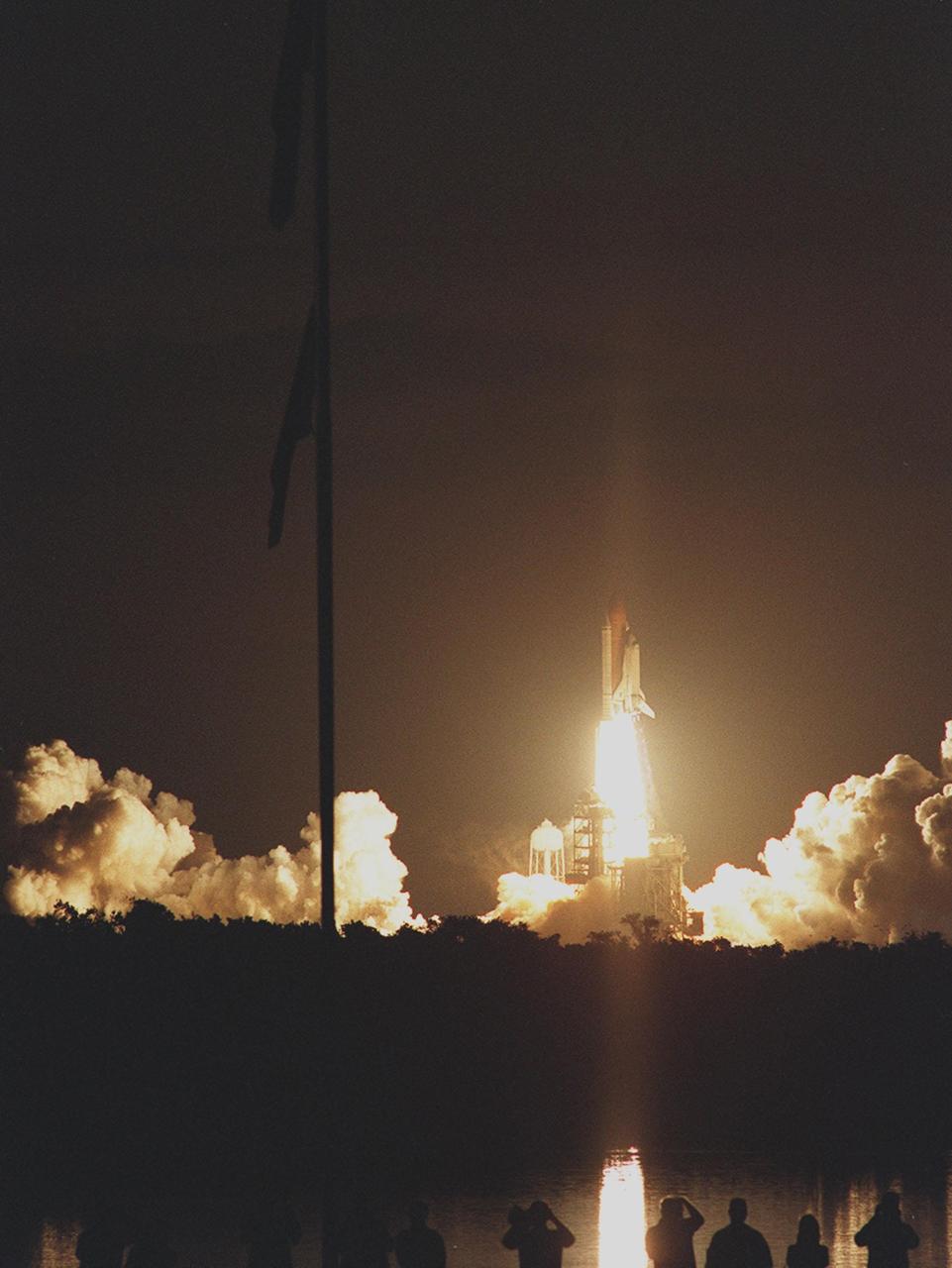 KENNEDY SPACE CENTER, Fla. --  In a burst of light, Space Shuttle Atlantis hurtles into the pre-dawn sky on mission STS-101 at 6:11:10 a.m. EDT. Silhouetted on the left are two American flags, hung from a flagpole near the Press Site bleachers. Media and spectators below have an unobstructed view across the turn basin, which reflects the fiery liftoff. The mission is taking the crew of seven to the International Space Station to deliver logistics and supplies as well as to prepare the Station for the arrival of the Zvezda Service Module, expected to be launched by Russia in July 2000. Also, the crew will conduct one space walk and will reboost the space station from 230 statute miles to 250 statute miles. This will be the third assembly flight to the Space Station. After a 10-day mission, landing is targeted for May 29 at 2:19 a.m. EDT. This is the 98th Shuttle flight and the 21st flight for Shuttle Atlantis