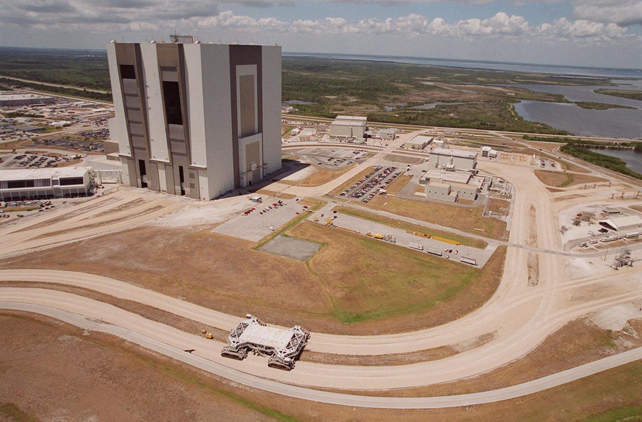 This aerial photo captures many of the facilities involved in Space Shuttle processing. At center is the Vehicle Assembly Building (VAB). The curved road in the foreground is the newly restored crawlerway leading into the VAB high bay 2. The road restoration and high bay 2 are part of KSC’s Safe Haven project, enabling the storage of orbiters during severe weather. The road circles around the Orbiter Processing Facility 3 (OPF-3) at right center. OPF1 and OPF-2 are just above the curving road. On the left of the VAB, the crawlerway also extends from high bays 1 and 3, past the Launch Control Center, out to the two Shuttle launch pads