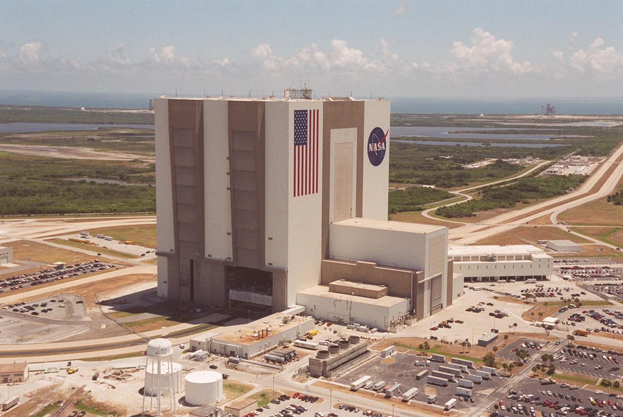 This aerial photo captures many of the facilities involved in Space Shuttle launches. At center is the Vehicle Assembly Building (VAB). The curved road on the near side is the newly restored crawlerway leading into the VAB high bay 2, where a mobile launcher platform/crawler-transporter currently sits. The road restoration and high bay 2 are part of KSC’s Safe Haven project, enabling the storage of orbiters during severe weather. The crawlerway also extends from the east side of the VAB out to the two Space Shuttle launch pads. In the distance is the Atlantic Ocean