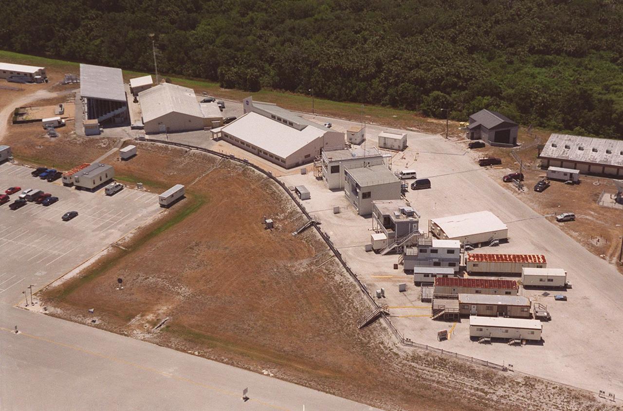 This aerial view is of the buildings that comprise the NASA Press Site in the Launch Complex 39 area. The first large building on the left is the grandstand from which media representatives view the Space Shuttle launches. The building next to it houses the auditorium from which NASA press briefings are broadcast. To its immediate right is the NASA News Center which includes the offices of the NASA spokesmen at Kennedy Space Center. The buildings and trailers to the right of the News Center are assigned to various television stations and news services
