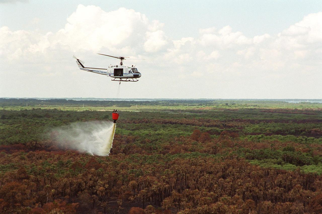 A NASA helicopter drops water from a special “bucket” onto a small fire on Kennedy Space Center grounds. The site is between Kennedy Parkway North and the Indian River. The fire is one of many throughout Central Florida, which is suffering from drought