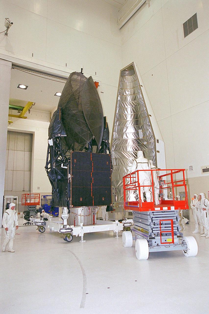 In the Spacecraft Assembly and Encapsulation Facility, the Tracking and Data Relay Satellite (TDRS-H) at left is ready for encapsulation. Workers in an extendable platform wait for the fairing (right) to move into place. After encapsulation in the fairing, TDRS will be transported to Launch Pad 36A, Cape Canaveral Air Force Station for launch scheduled June 29 aboard an Atlas IIA/Centaur rocket. One of three satellites (labeled H, I and J) being built in the Hughes Space and Communications Company Integrated Satellite Factory in El Segundo, Calif., the latest TDRS uses an innovative springback antenna design. A pair of 15-foot-diameter, flexible mesh antenna reflectors fold up for launch, then spring back into their original cupped circular shape on orbit. The new satellites will augment the TDRS system’s existing Sand Ku-band frequencies by adding Ka-band capability. TDRS will serve as the sole means of continuous, high-data-rate communication with the space shuttle, with the International Space Station upon its completion, and with dozens of unmanned scientific satellites in low earth orbit
