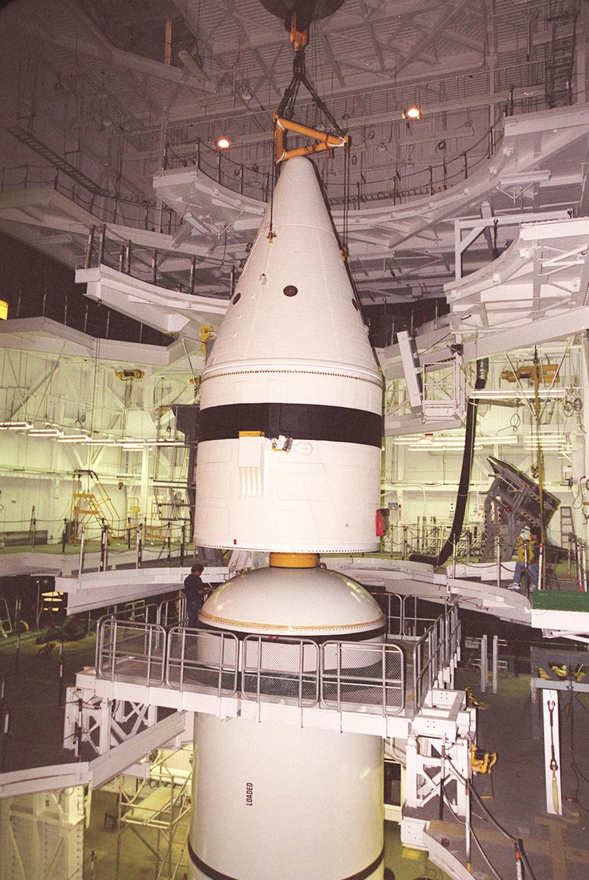 Inside the Vehicle Assembly Building, an overhead crane lowers the forward section of a solid rocket booster (SRB) toward the rest of the stack for mating. The forward section of each booster, from nose cap to forward skirt contains avionics, a sequencer, forward separation motors, a nose cone separation system, drogue and main parachutes, a recovery beacon, a recovery light, a parachute camera on selected flights and a range safety system. Each SRB weighs approximately 1.3 million pounds at launch. The SRB is part of the stack for Space Shuttle Discovery and the STS-92 mission, scheduled for launch Oct. 5, from Launch Pad 39A, on the fifth flight to the International Space Station