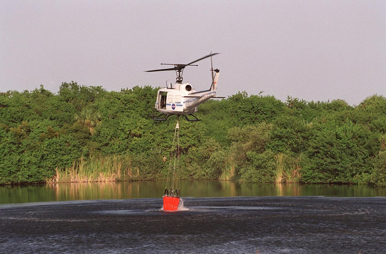 A NASA helicopter dips its fire-fighting bucket into the river to pick up and deliver a cargo of water to a wildfire at KSC. Before being extinguished, the fire burned about 20 acres at a site near gate 2C on Kennedy Parkway North (route 3)