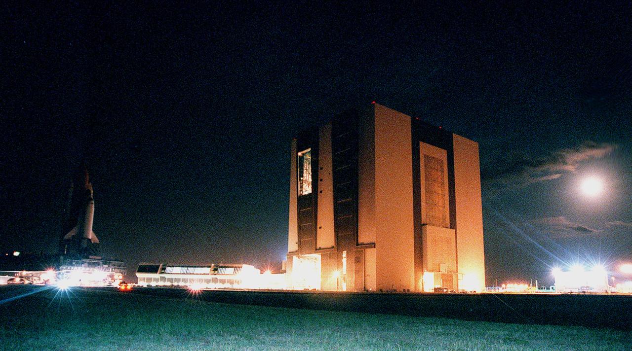 KENNEDY SPACE CENTER, FLA. -- This 30-second timed exposure captures the bright lights around the Vehicle Assembly Building (VAB) plus the equally bright moon (upper right) as Space Shuttle Atlantis (far left) rolls out of the east side bay 1.  The Launch Control Center sits between the Shuttle and the VAB.  The full stack of Shuttle, solid rocket boosters and external tank are taking part in a fit check for the newly renovated crawlerway and high bay 2, which is on the west side.  The major modifications to the crawlerway and VAB provide Shuttle flight hardware more storage space and protection - "Safe Haven" - from hurricanes or tropical storms.  Atlantis began moving out of VAB high bay 1 at 2:59 a.m. EDT.  After the successful Safe Haven fit check, Shuttle Atlantis is scheduled to roll out to Launch Pad 39B in preparation for the STS-106 launch on Sept. 8.