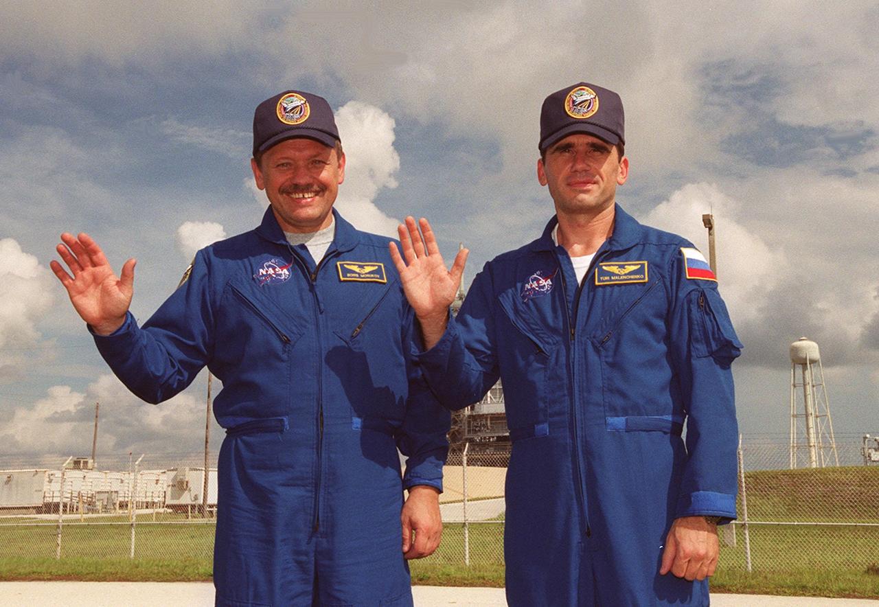 Russian cosmonauts Boris V. Morukov and Yuri I. Malenchenko wave for the photo while standing in front of Launch Pad 39B where Space Shuttle Atlantis awaits launch. The cosmonauts are with the Russian Aviation and Space Agency. STS-106 is scheduled to launch Sept. 8, 2000, at 8:45 a.m. EDT from Launch Pad 39B. On the 11-day mission, the seven-member crew will perform support tasks on orbit, transfer supplies and prepare the living quarters in the newly arrived Zvezda Service Module. Malenchenko will perform a six-and-a-half-hour space walk, along with Mission Specialist Edward T. Lu, during the mission. Landing is targeted for Sept. 19 at 4:59 a.m. EDT at the KSC Shuttle Landing Facility
