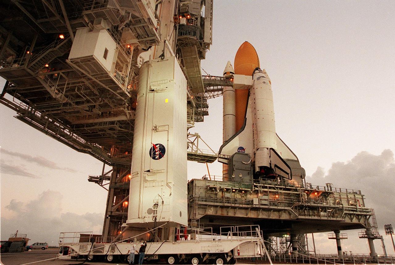 KENNEDY SPACE CENTER, Fla. --  With the onset of dawn, the payload canister (left) with the Integrated Truss Structure Z1 inside begins its journey up the side of the Rotating Service Structure to the Payload Changeout Room. There the Z1 truss will be removed and later transferred to Space Shuttle Discovery’s payload bay. The Z1 truss is the first of 10 that will become the backbone of the International Space Station, eventually stretching the length of a football field. Along with its companion payload, the third Pressurized Mating Adapter, the Z1 is scheduled to be launched aboard Discovery Oct. 5 at 9:38 p.m. EDT