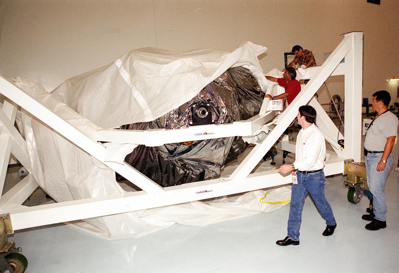 KENNEDY SPACE CENTER, FLA. -- Workers in the Space Station Processing Facility remove the cover from the Mobile Remote Servicer Base System (MBS), part of the Canadian Space Agency’s (CSA) Space Station Remote Manipulator System (SSRMS). The MBS is scheduled to be launched in February 2002 on flight UF-2 to the International Space Station. The MBS will complete the Canadian Mobile Servicing System, or MSS. The mechanical arm will have the capability to "inchworm" from the U.S. Lab fixture to the MSS and travel along the Truss to work sites on the Space Station