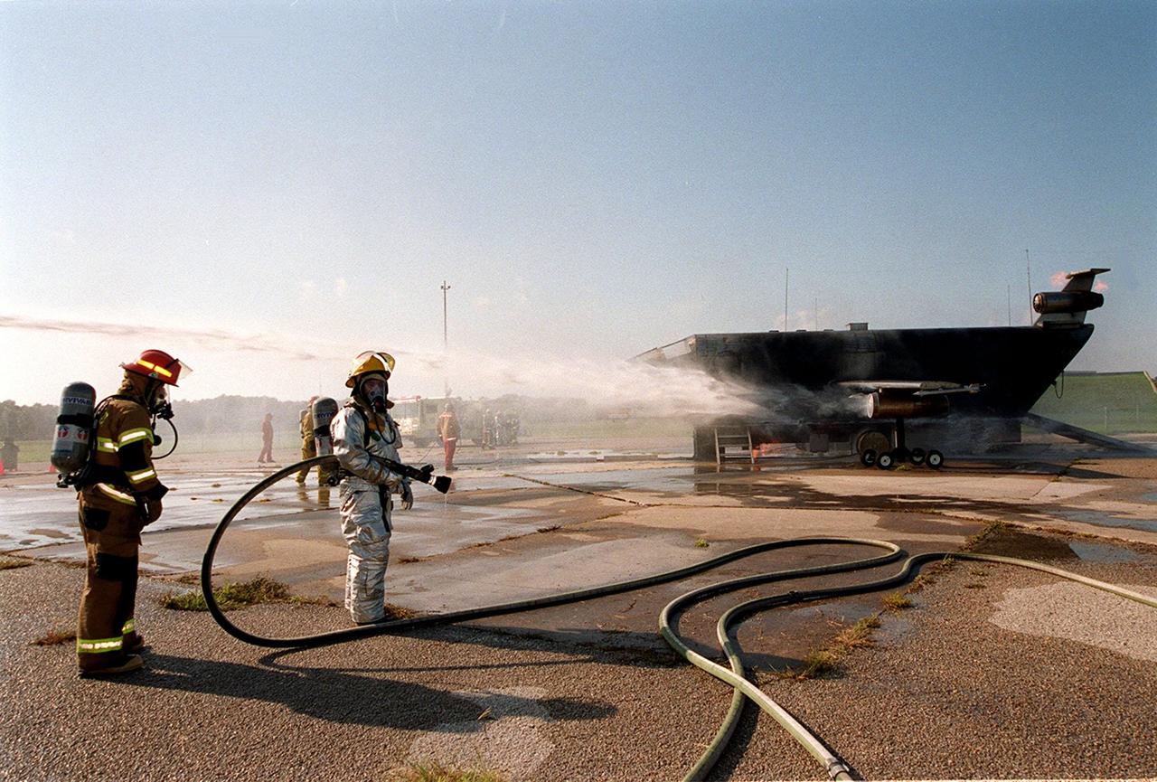KENNEDY SPACE CENTER, FLA. --  Firefighters in full gear wait to approach a burning simulated aircraft during training exercises at Cape Canaveral Air Force Station Pad 30. The firefighters are with the Fire and Emergency Services at the Naval Station Mayport, Fla.
