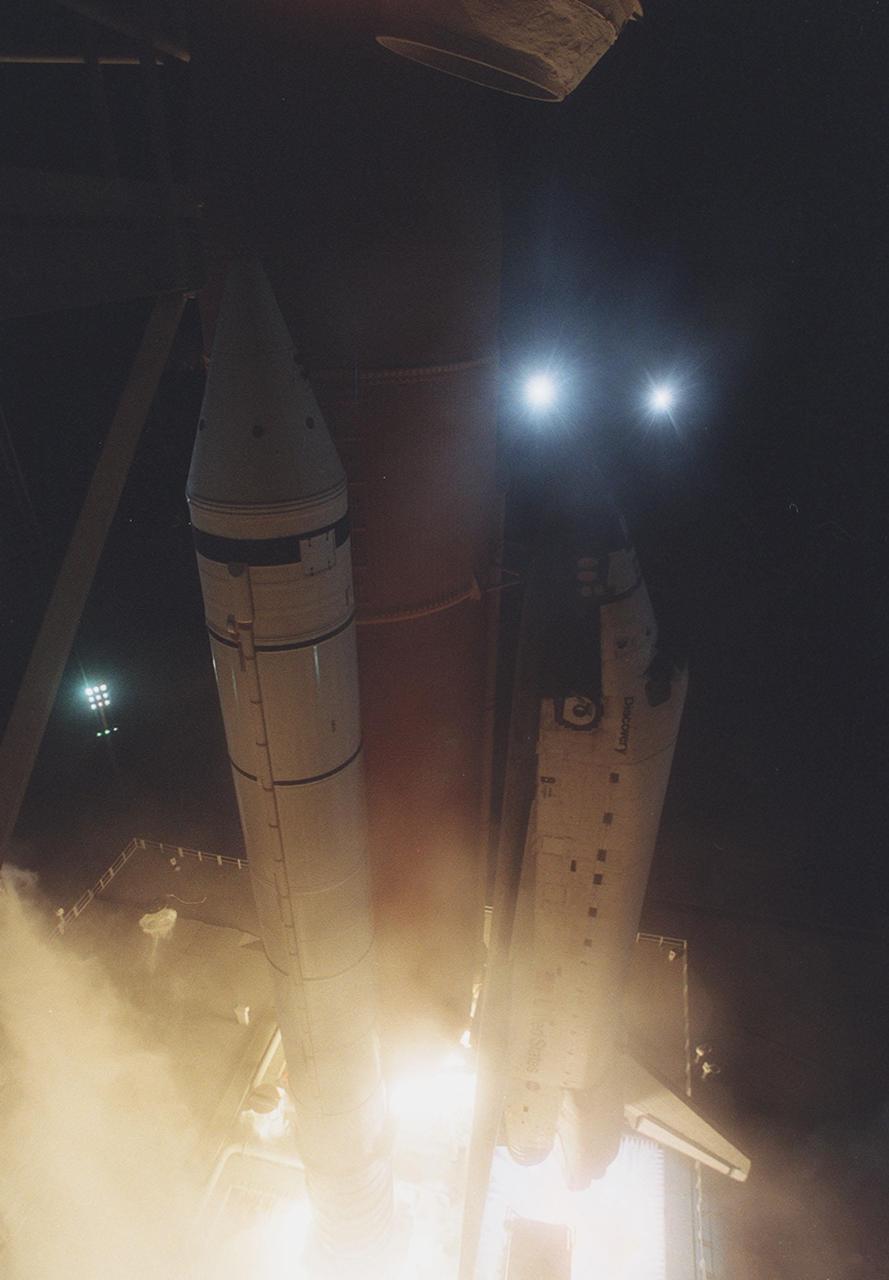 KENNEDY SPACE CENTER, Fla. -- Space Shuttle Discovery lifts off Launch Pad 39A against a backdrop of xenon lights (just above the orbiter’ nose and at left). On the Mobile Launcher Platform beneath, water begins flooding the area for flame and sound control. The perfect on-time liftoff occurred at 7:17 p.m. EDT, sending a crew of seven on the 100th launch in the history of the Shuttle program. Discovery carries a payload that includes the Integrated Truss Structure Z-1, first of 10 trusses that will form the backbone of the Space Station, and the third Pressurized Mating Adapter that will provide a Shuttle docking port for solar array installation on the sixth Station flight and Lab installation on the seventh Station flight. Discovery’s landing is expected Oct. 22 at 2:10 p.m. EDT