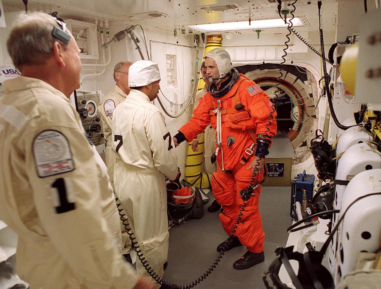 STS-92 Mission Specialist Peter J.K. “Jeff” Wisoff reaches out to shake the hand of Danny Wyatt, KSC NASA Quality Assurance specialist, after completing final check of his launch and entry suit in the White Room before entering Discovery. The White Room is an environmentally controlled area at the end of the Orbiter Access Arm that provides entry to the orbiter as well as emergency egress if needed. The arm remains in the extended position until 7 minutes 24 seconds before launch. Wisoff and the rest of the crew are undertaking the fifth flight to the International Space Station for construction. Discovery carries a payload that includes the Integrated Truss Structure Z-1, first of 10 trusses that will form the backbone of the Space Station, and the third Pressurized Mating Adapter that will provide a Shuttle docking port for solar array installation on the sixth Station flight and Lab installation on the seventh Station flight. The mission includes four spacewalks for the construction activities. Discovery’s landing is expected Oct. 22 at 2:10 p.m. EDT