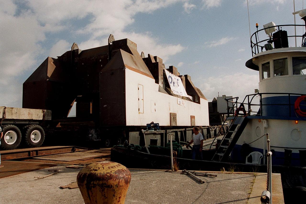 A launch table fabricated by Jered Industries in Georgia is ready for transfer to Launch Complex 37B, Cape Canaveral Air Force Station, after being stabilized aboard the barge that brought it to the turn basin in KSC’s Launch Complex 39 Area. In the background is the Vehicle Assembly Building. The table was built in support of the Delta Evolved Expendable Launch Vehicle (EELV) program, known as Delta IV. It was floated on the barge down the Intercoastal Waterway, through the Barge Canal to the turn basin. The table is approximately 70 feet long, 40 feet wide and 50 feet high, and weighs about 600,000 pounds. Accompanying the launch table on the barge are flame deflectors, which are also to be erected on pad 37B