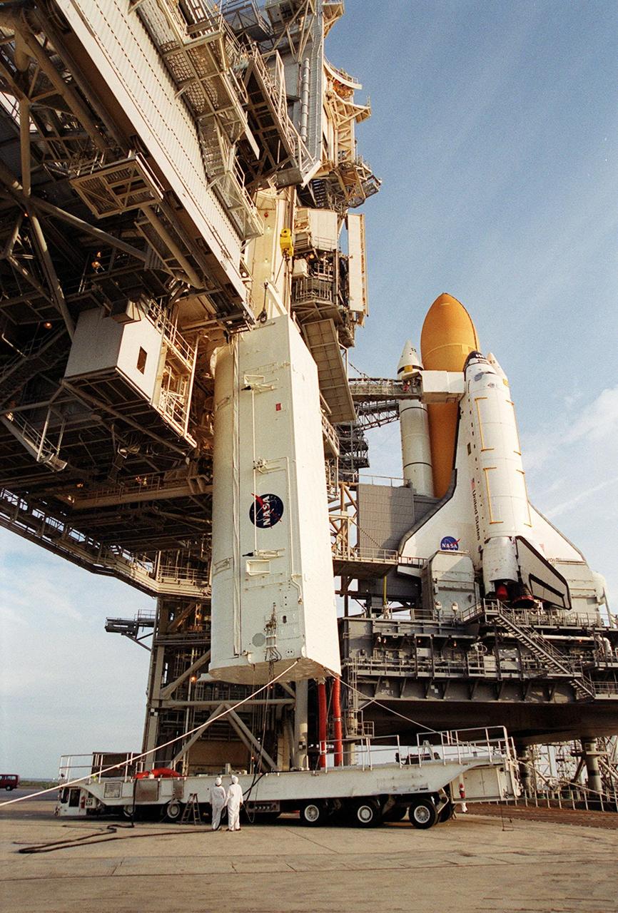 KENNEDY SPACE CENTER, FLA. -- On Launch Pad 39B, the payload transport canister, with the P6 integrated truss segment inside, is lifted toward the payload changeout room (PCR). The PCR is the enclosed, environmentally controlled portion of the Rotating Service Structure (RSS) (on the left) that supports payload delivery at the pad. At right is Space Shuttle Endeavour with its orange external tank and one solid rocket booster showing behind it. When the RSS is closed around Endeavour, the P6 truss will be able to be moved into the orbiter’s payload bay. The P6, payload on mission STS-97, comprises Solar Array Wing-3 and the Integrated Electronic Assembly, to be installed on the International Space Station. The Station’s electrical power system will use eight photovoltaic solar arrays, each 112 feet long by 39 feet wide, to convert sunlight to electricity. The solar arrays are mounted on a “blanket” that can be folded like an accordion for delivery. Once in orbit, astronauts will deploy the blankets to their full size. Gimbals will be used to rotate the arrays so that they will face the Sun to provide maximum power to the Space Station. Launch of STS-97 is scheduled for Nov. 30 at 10:06 p.m. EST