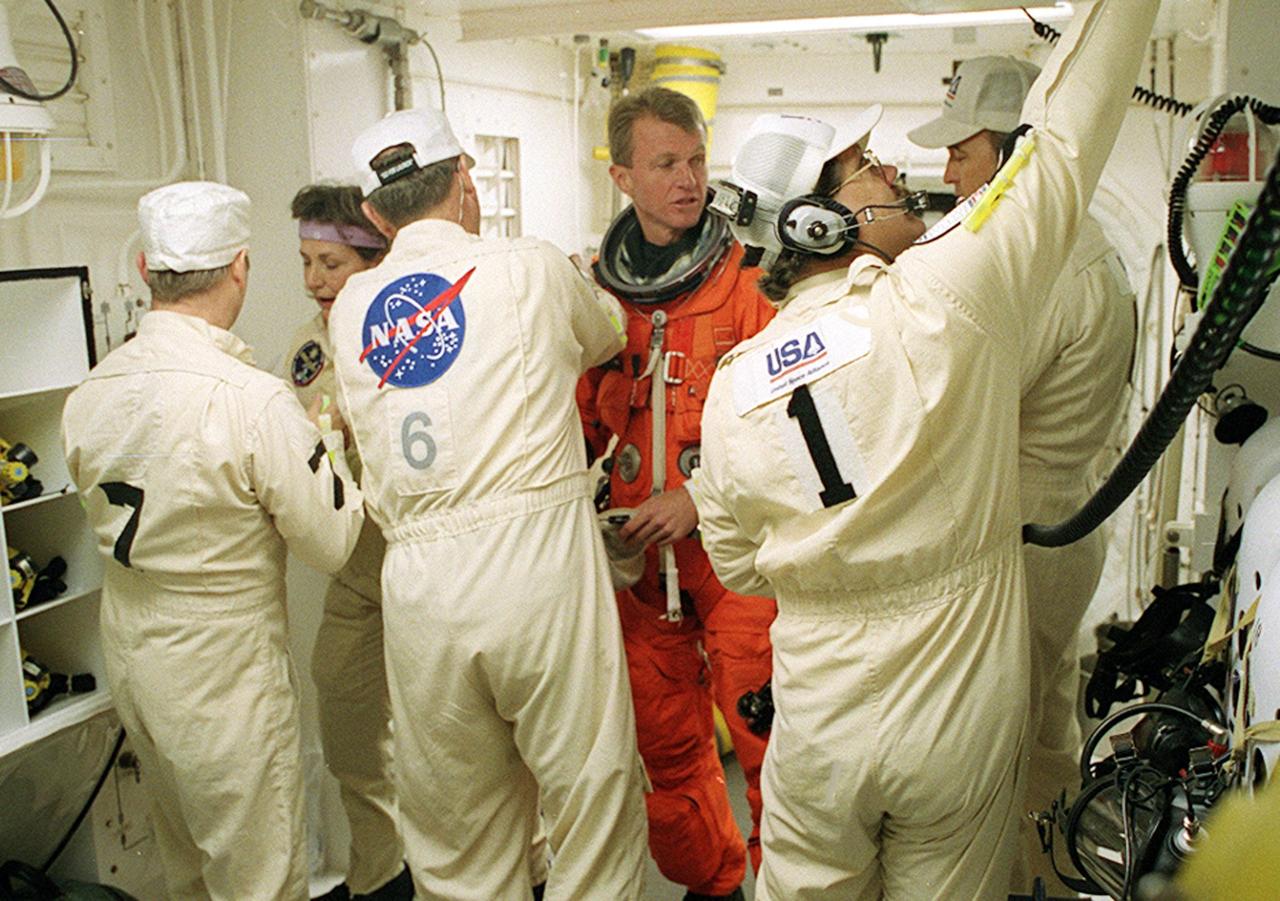 In the White Room, STS-97 Commander Brent Jett (center) prepares for entry into Space Shuttle Endeavour with the help of the Closeout Crew, (left to right) Mike Birkenseher, Jean Alexander, Jack Burritt, Travis Thompson and Dave Law. Space Shuttle Endeavour is targeted to launch Nov. 30 at 10:06 p.m. EST for the six construction flight to the International Space Station. Endeavour is transporting the P6 Integrated Truss Structure that comprises Solar Array Wing-3 and the Integrated Electronic Assembly, to provide power to the Space Station. After the 11-day mission, which includes three spacewalks, it is expected to land at KSC Dec. 11 at 6:19 p.m. EST