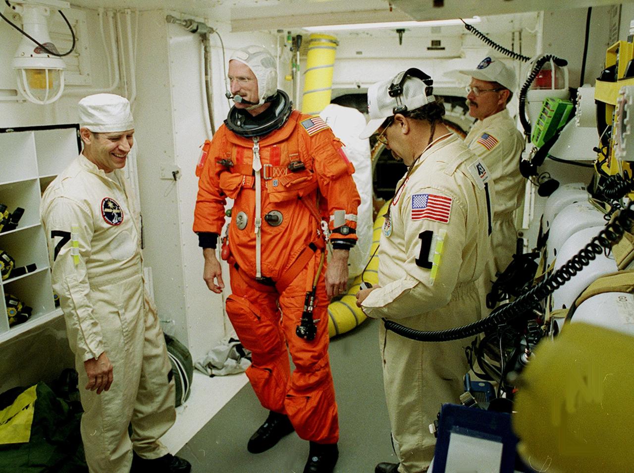 In the White Room, STS-97 Mission Specialist Joseph Tanner prepares for entry into Space Shuttle Endeavour with the help of the Closeout Crew, Mike Birkenseher (left), Travis Thompson (right, foreground) and Jack Burritt (right, background). Space Shuttle Endeavour is targeted to launch Nov. 30 at 10:06 p.m. EST for the six construction flight to the International Space Station. Endeavour is transporting the P6 Integrated Truss Structure that comprises Solar Array Wing-3 and the Integrated Electronic Assembly, to provide power to the Space Station. After the 11-day mission, which includes three spacewalks, it is expected to land at KSC Dec. 11 at 6:19 p.m. EST