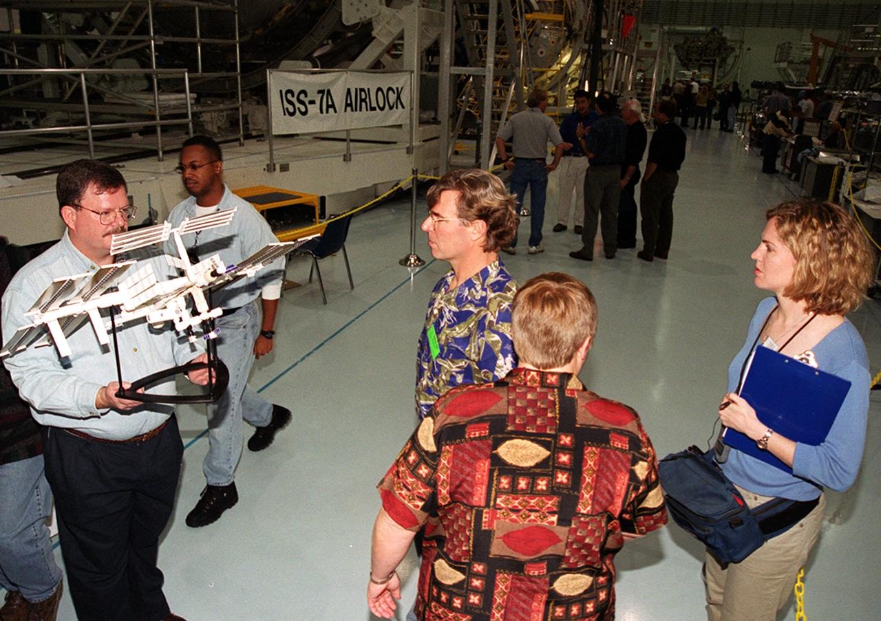 KENNEDY SPACE CENTER, FLA. -- In the Space Station Processing Facility, Steve Thomas (center), looks at a model of the International Space Station being held by a worker. Thomas is host of the television series "This Old House." In the foreground and at right are crew members of the television series.; They are at KSC to film an episode of the series