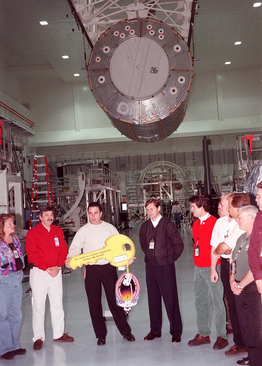 KENNEDY SPACE CENTER, FLA. -- In the Space Station Processing Facility, the “key” to the U.S. Laboratory Destiny is officially handed over to NASA during a brief ceremony while workers look on. Suspended overhead is the laboratory, being moved to the Launch Package Integration Stand (LPIS) for a weight and center of gravity determination. Destiny is the payload aboard Space Shuttle Atlantis on mission STS-98 to the International Space Station. The lab is fitted with five system racks and will already have experiments installed inside for the flight. The launch is scheduled for January 2001