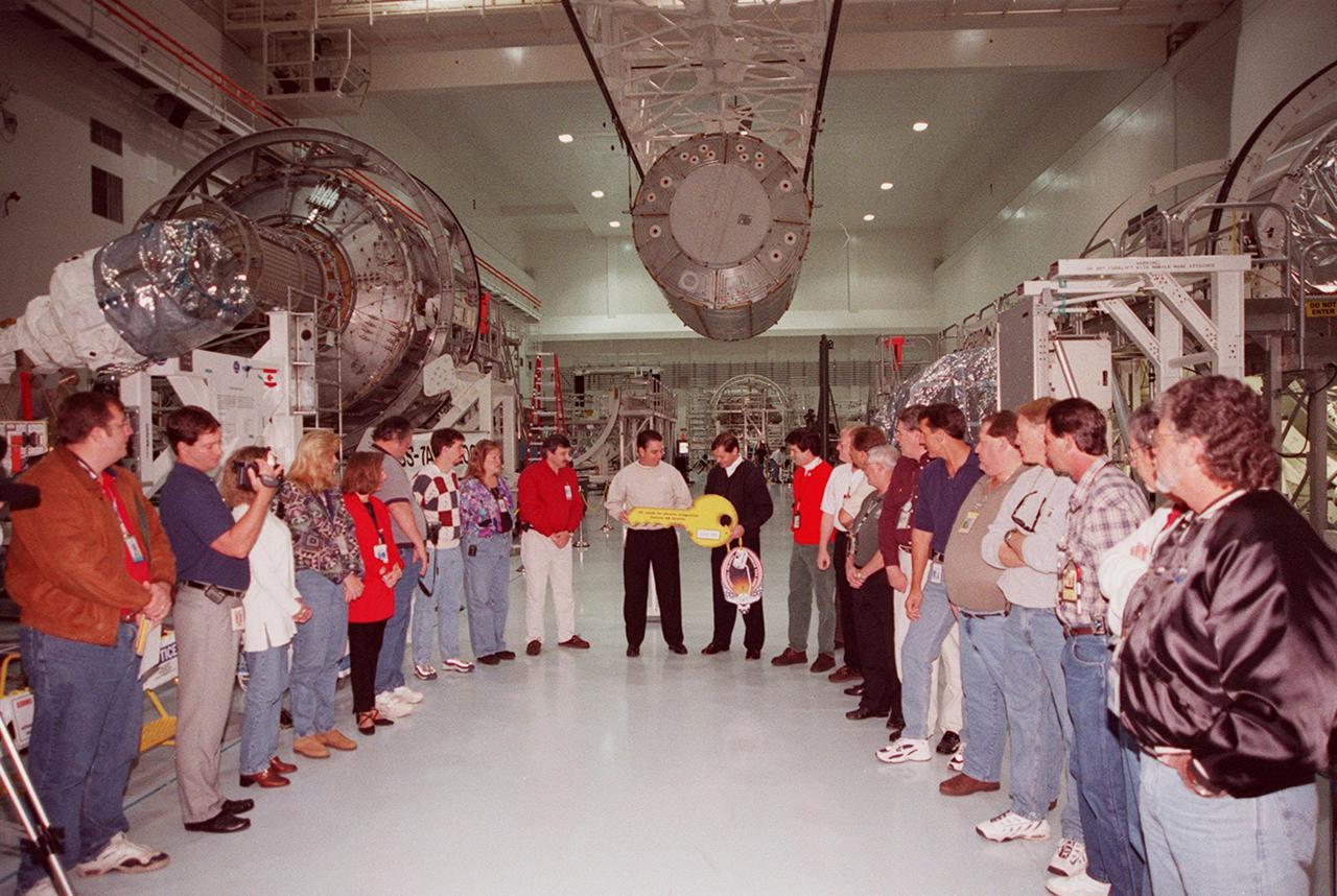 KENNEDY SPACE CENTER, FLA. -- In the Space Station Processing Facility, the “key” to the U.S. Laboratory Destiny is officially handed over to NASA during a brief ceremony while workers look on. Suspended overhead is the laboratory, being moved to the Launch Package Integration Stand (LPIS) for a weight and center of gravity determination. Behind the workers at left is the Joint Airlock Module. Destiny is the payload aboard Space Shuttle Atlantis on mission STS-98 to the International Space Station. The lab is fitted with five system racks and will already have experiments installed inside for the flight. The launch is scheduled for January 2001