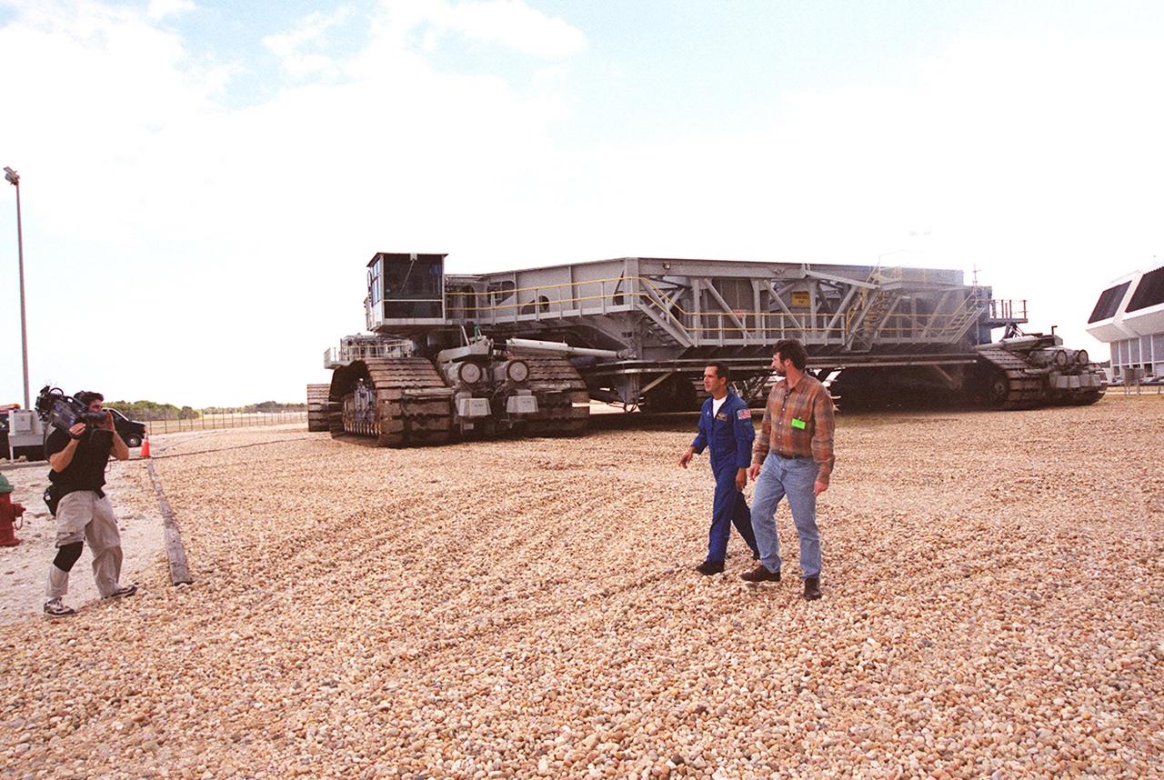 Astronaut John Herrington (center) and master carpenter on This Old House, Norm Abram, are filmed walking in front of a crawler-transporter near the Launch Control Center (far right). The cast and crew of This Old House are filming at KSC for an episode of the show. Herrington is accompanying the film crew on their tour of KSC