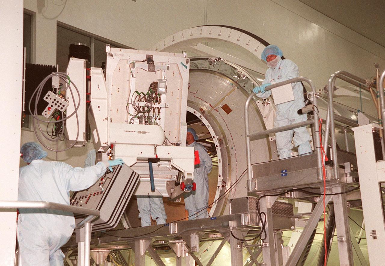 KENNEDY SPACE CENTER, FLA. -- Workers (right, left and center) in the Space Station Processing Facility wait to install a laboratory rack in the Multi-Purpose Logistics Module Leonardo (background). Leonardo is the first of three such pressurized modules that will serve as the International Space Station's “moving vans,” carrying laboratory racks filled with equipment, experiments and supplies to and from the Space Station aboard the Space Shuttle. Approximately 21 feet long and 15 feet in diameter, Leonardo will be launched on Shuttle mission STS-102 March 1, 2001. On that flight, Leonardo will be filled with equipment and supplies to outfit the U.S. laboratory module, being carried to the ISS on the Jan. 19, 2001, launch of STS-98