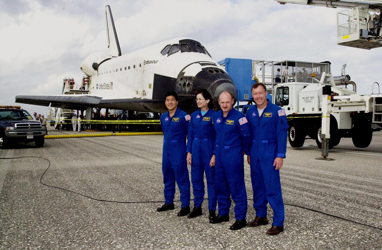 KENNEDY SPACE CENTER, FLA. --  After a successful return to Earth aboard orbiter Endeavour (background), the STS-108 crew pose for a photo.  From left are Mission Specialists Daniel M. Tani and Linda A. Godwin, Pilot Mark E. Kelly and Commander Dominic L. Gorie.  The mission had an elapsed time of 11 days, 19 hours and 35 minutes. Main gear touchdown occurred at 12:55:10 p.m. EST (17:55:10 GMT), nose gear touchdown at 12:55:23 p.m. (17:55:23 GMT) , wheel stop at 12:56:13 p.m. (17:56:13 GMT).   STS-108 was the 12th mission to the International Space Station.  This mission was the 107th flight in the Shuttle program and the 17th flight for the orbiter. The landing is the 57th at KSC in the history of the program. Endeavour carried both the mission crew and the Expedition 3 crew - Commander Frank Culbertson and cosmonauts Vladimir Dezhurov and Mikhail Tyurin - who returned to Earth after 129 days in space on the Space Station