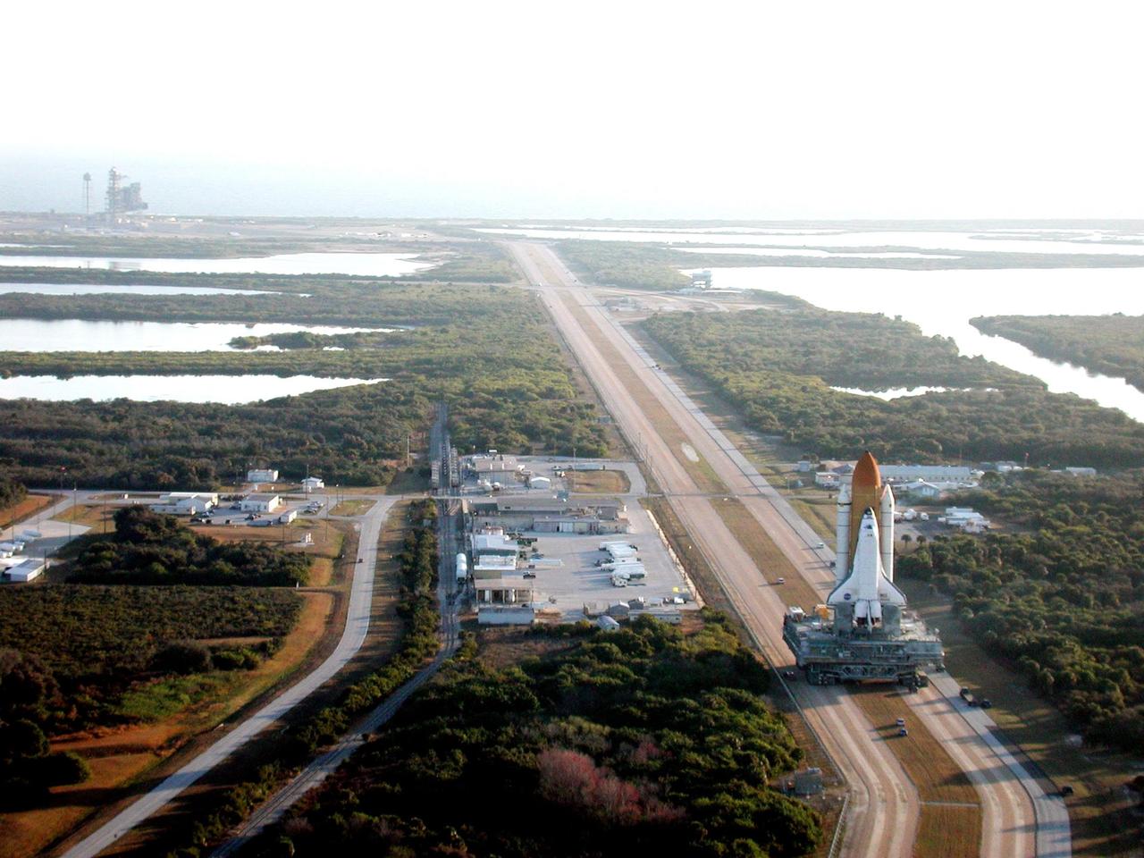 KENNEDY SPACE CENTER, Fla. -- As the early morning light casts a glow over the landscape, Space Shuttle Atlantis moves slowly along the crawlerway for the trek to Launch Pad 39A (upper left). The Shuttle has been in the VAB undergoing tests on the solid rocket booster cables. A prior extensive evaluation of NASA’s SRB cable inventory on the shelf revealed conductor damage in four (of about 200) cables. Shuttle managers decided to prove the integrity of the system tunnel cables already on Atlantis, causing return of the Shuttle to the VAB a week ago. Launch of Atlantis on STS-98 has been rescheduled to Feb. 7 at 6:11 p.m. EST
