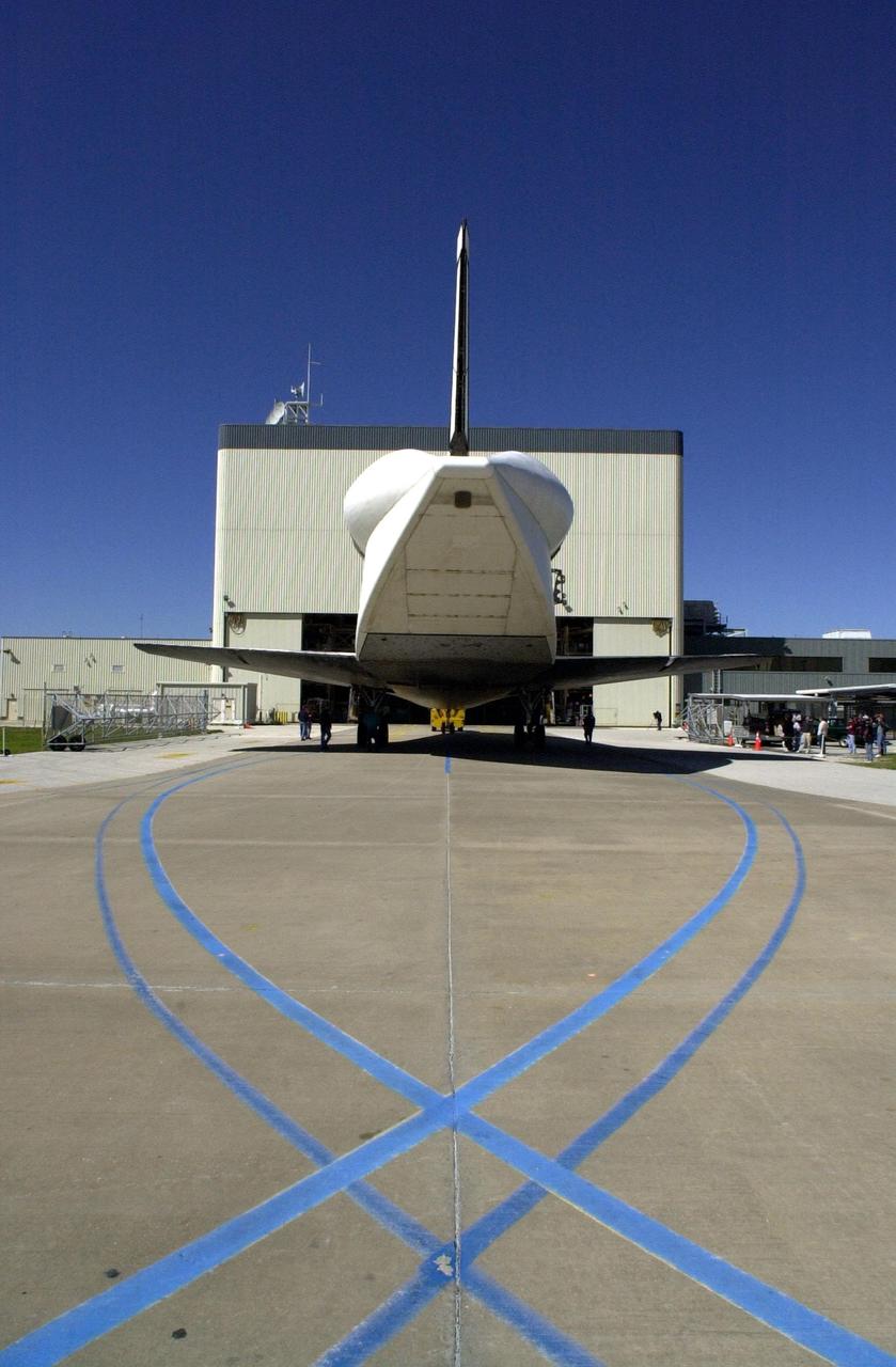 Viewed from the rear, the orbiter Atlantis heads toward the open doors of the Orbiter Processing Facility bay 3 after being towed from the Shuttle Landing Facility. The blue lines represent the orbiter’s turning lines into and away from bay 3. The unusual silhouette of the aft section on the orbiter is due to the tail cone covering the aft engines. Atlantis landed Feb. 19 at Edwards Air Force Base concluding mission STS-98. The orbiter returned to Florida on the back of a Shuttle Carrier Aircraft, known as a ferry flight, that began March 1. Unfavorable weather conditions kept it on the ground at Altus AFB, Okla., for several days until it could return to Florida. Atlantis will be prepared in the OPF for mission STS-104, the 10th construction flight to the International Space Station, scheduled to launch June 8
