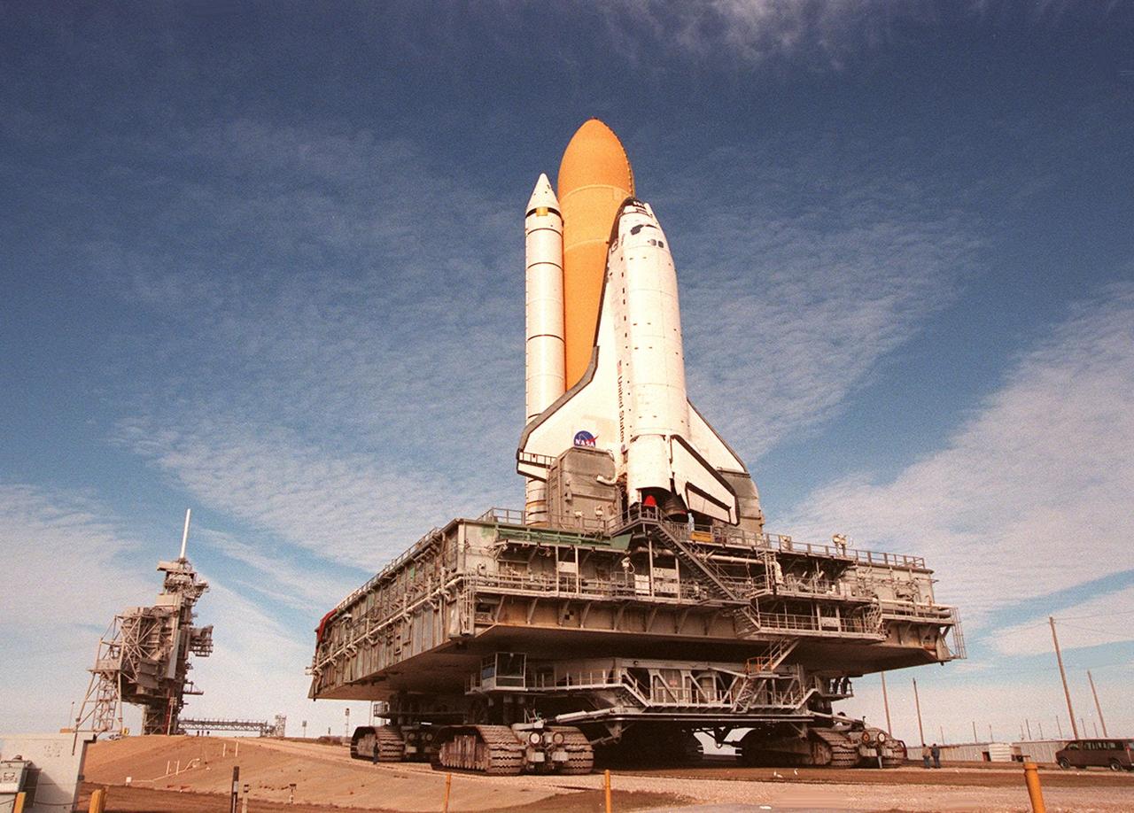 KENNEDY SPACE CENTER, Fla. -- Under wispy white clouds, Space Shuttle Atlantis slowly moves toward the Rotating and Fixed Service Structures on Launch Pad 39A. The 80-foot-tall white lighting mast is seen atop the FSS. Atlantis will fly on mission STS-98, the seventh construction flight to the International Space Station, carrying the U.S. Laboratory, named Destiny. The lab will have five system racks already installed inside the module. After delivery of electronics in the lab, electrically powered attitude control for Control Moment Gyroscopes will be activated. Atlantis is scheduled for launch no earlier than Jan. 19, 2001, with a crew of five