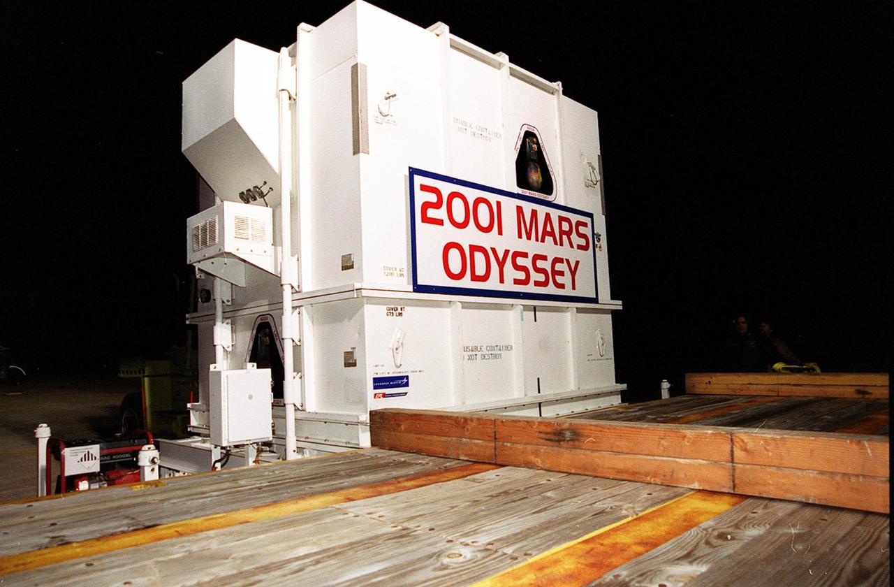The 2001 Mars Odyssey spacecraft sits on the bed of the trailer that will take it from KSC’s Shuttle Landing Facility to the Spacecraft Assembly and Encapsulation Facility 2 (SAEF-2) located in the KSC Industrial Area. The spacecraft arrived at the SLF aboard an Air Force C-17 cargo airplane that brought it from Denver, Colo.., location of the Lockheed Martin plant where the spacecraft was built. In the SAEF Odyssey will undergo final assembly and checkout. This includes installation of two of the three science instruments, integration of the three-panel solar array, and a spacecraft functional test. It will be fueled and then mated to an upper stage booster, the final activities before going to the launch pad. Launch is planned for April 7, 2001 the first day of a 21-day planetary window. Mars Odyssey will be inserted into an interplanetary trajectory by a Boeing Delta II launch vehicle from Pad A at Complex 17 at the Cape Canaveral Air Force Station, Fla. The spacecraft will arrive at Mars on Oct. 20, 2001, for insertion into an initial elliptical capture orbit. Its final operational altitude will be a 250-mile-high, Sun-synchronous polar orbit. Mars Odyssey will spend two years mapping the planet's surface and measuring its environment
