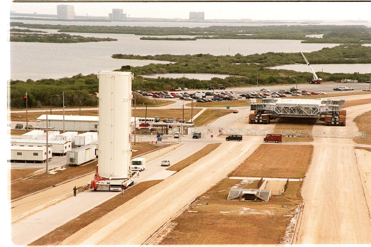 KENNEDY SPACE CENTER, FLA. -- An empty payload canister moves slowly to Launch Pad 39B alongside the crawlerway. In the near background is a crawler-transporter. Across the water, on the horizon can be seen buildings on the launch complexes at Cape Canaveral Air Force Station