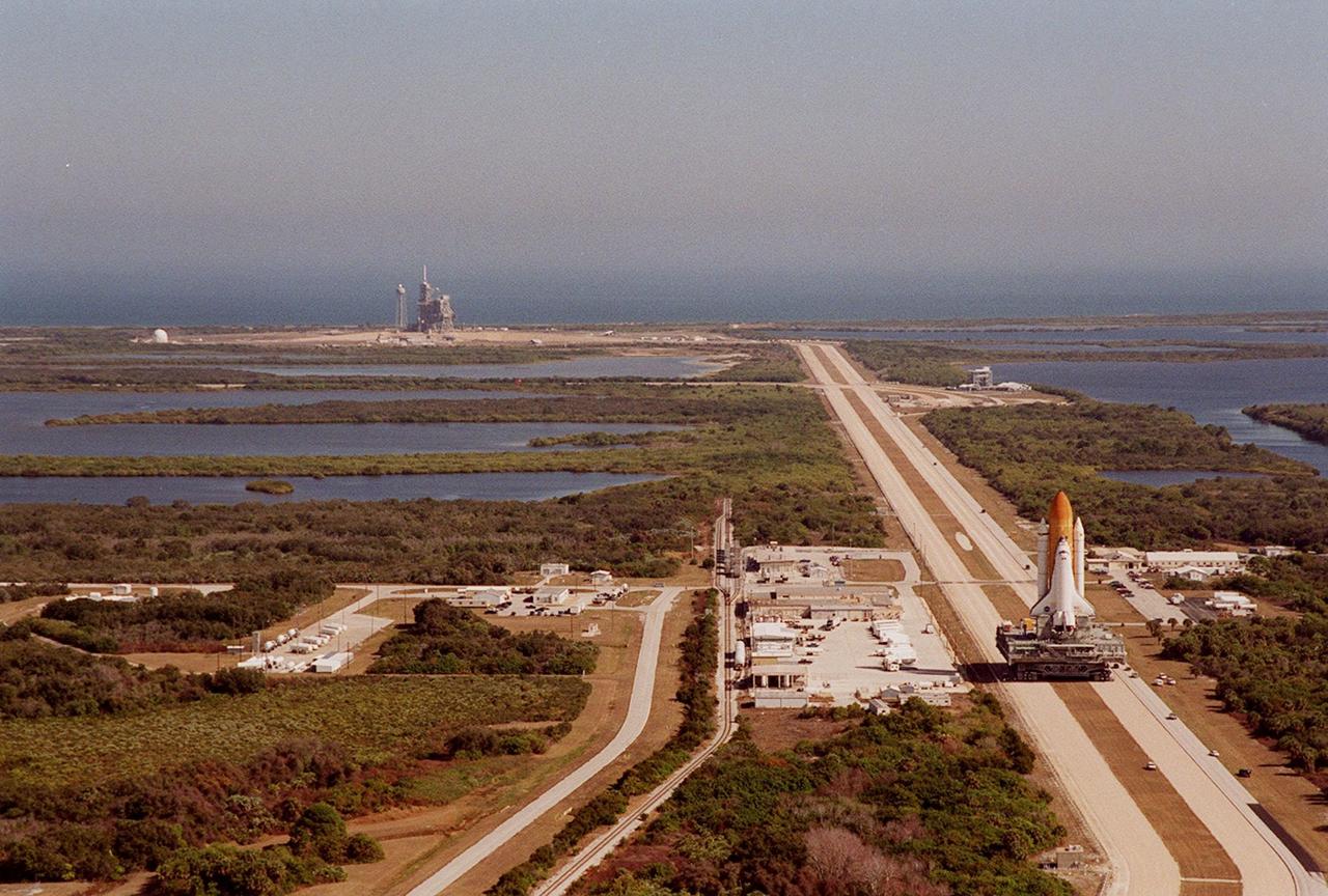KENNEDY SPACE CENTER, FLA. -- Space Shuttle <a href="../../subjects/atlantis.htm"> Atlantis</a> (right) inches its way at 1 mph atop the crawler-transporter back to the <a href="../../subjects/vab.htm"> Vehicle Assembly Building</a> from <a href="../../subjects/lc39a.htm"> Launch Pad 39A</a> (upper left). A panorama view from the top of the VAB shows the proximity of the pad to the Atlantic Ocean (background) plus the 3.4-mile crawlerway leading from the pad to the VAB. The water areas on both sides of the crawlerway are part of the Banana River. In the VAB workers will conduct inspections, make continuity checks and conduct X-ray analysis on the 36 solid rocket booster cables located inside each booster’s external system tunnel. An extensive evaluation of NASA’s SRB cable inventory revealed conductor damage in four (of about 200) cables on the shelf. Shuttle managers decided to prove the integrity of the system tunnel cables already on Atlantis before launching. The launch has been rescheduled no earlier than Feb. 6