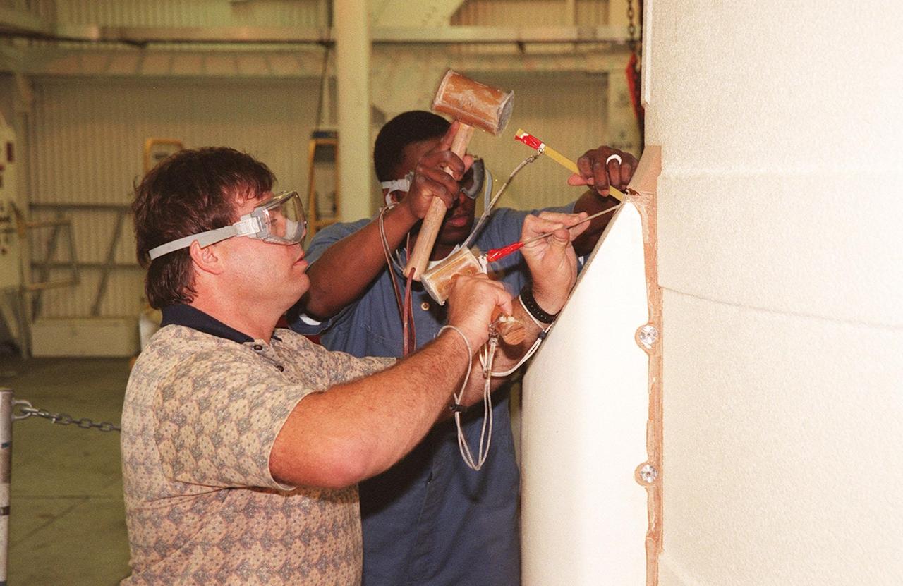 KENNEDY SPACE CENTER, FLA. -- In the Vehicle Assembly Building, Richard Bruns and Henry Jones, United Space Alliance SRB technicians, begin to detach the SRB system tunnel cover on the 36 cables inside. The SRB is part of Space Shuttle Atlantis, rolled back from Launch Pad 39A in order to conduct tests on the cables. A prior extensive evaluation of NASA’s SRB cable inventory on the shelf revealed conductor damage in four (of about 200) cables. Shuttle managers decided to prove the integrity of the system tunnel cables already on Atlantis before launching. Workers are conducting inspections, making continuity checks and conducting X-ray analysis on the cables. The launch has been rescheduled no earlier than Feb. 6. <br