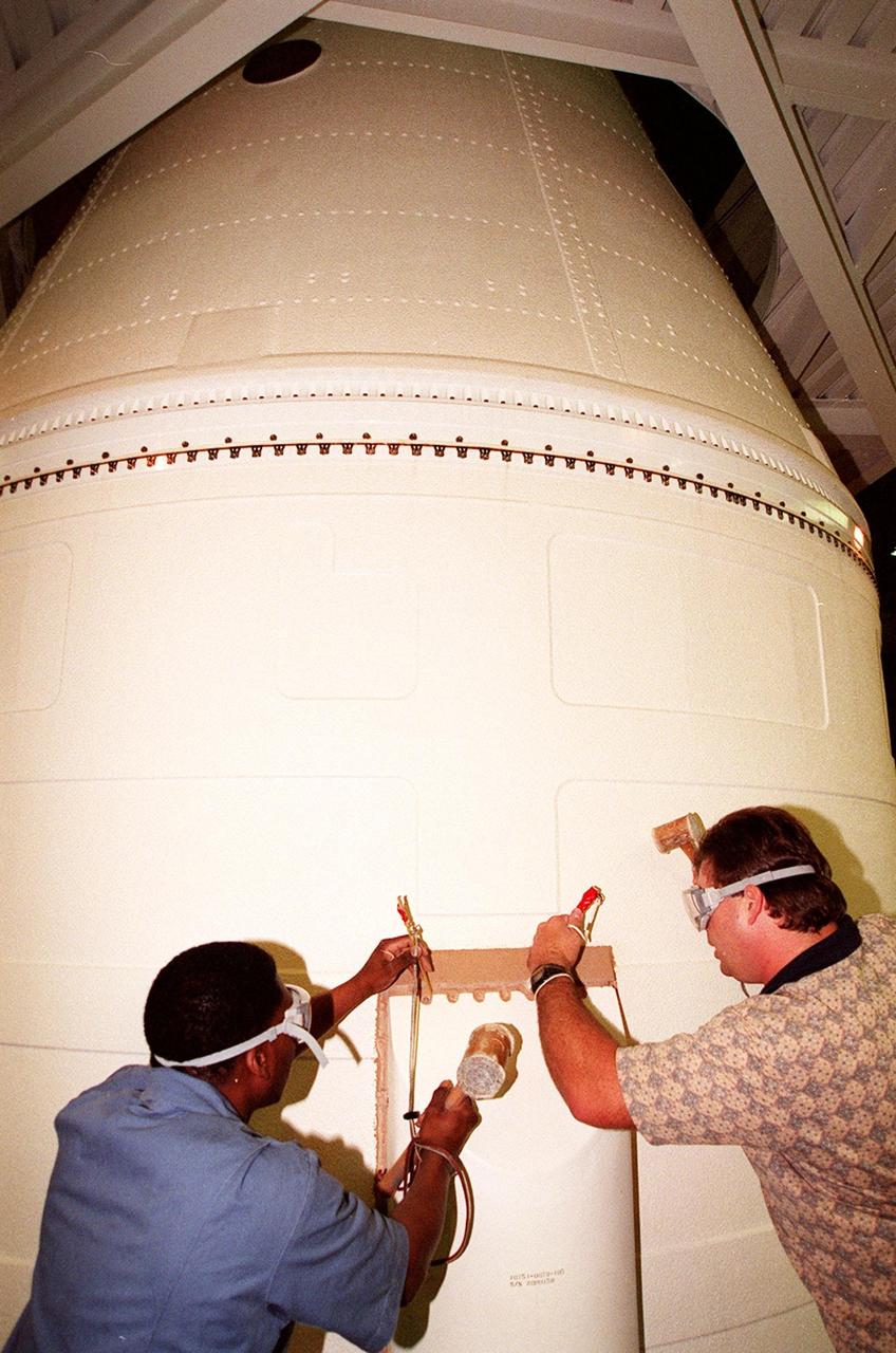 KENNEDY SPACE CENTER, FLA. -- In the Vehicle Assembly Building, near the top of the solid rocket booster, Henry Jones and Richard Bruns begin to detach the SRB system tunnel cover on the 36 cables inside. Jones and Bruns are United Space Alliance SRB technicians. The SRB is part of Space Shuttle Atlantis, rolled back from Launch Pad 39A in order to conduct tests on the cables. A prior extensive evaluation of NASA’s SRB cable inventory on the shelf revealed conductor damage in four (of about 200) cables. Shuttle managers decided to prove the integrity of the system tunnel cables already on Atlantis before launching. Workers are conducting inspections, making continuity checks and conducting X-ray analysis on the cables. The launch has been rescheduled no earlier than Feb. 6.<br