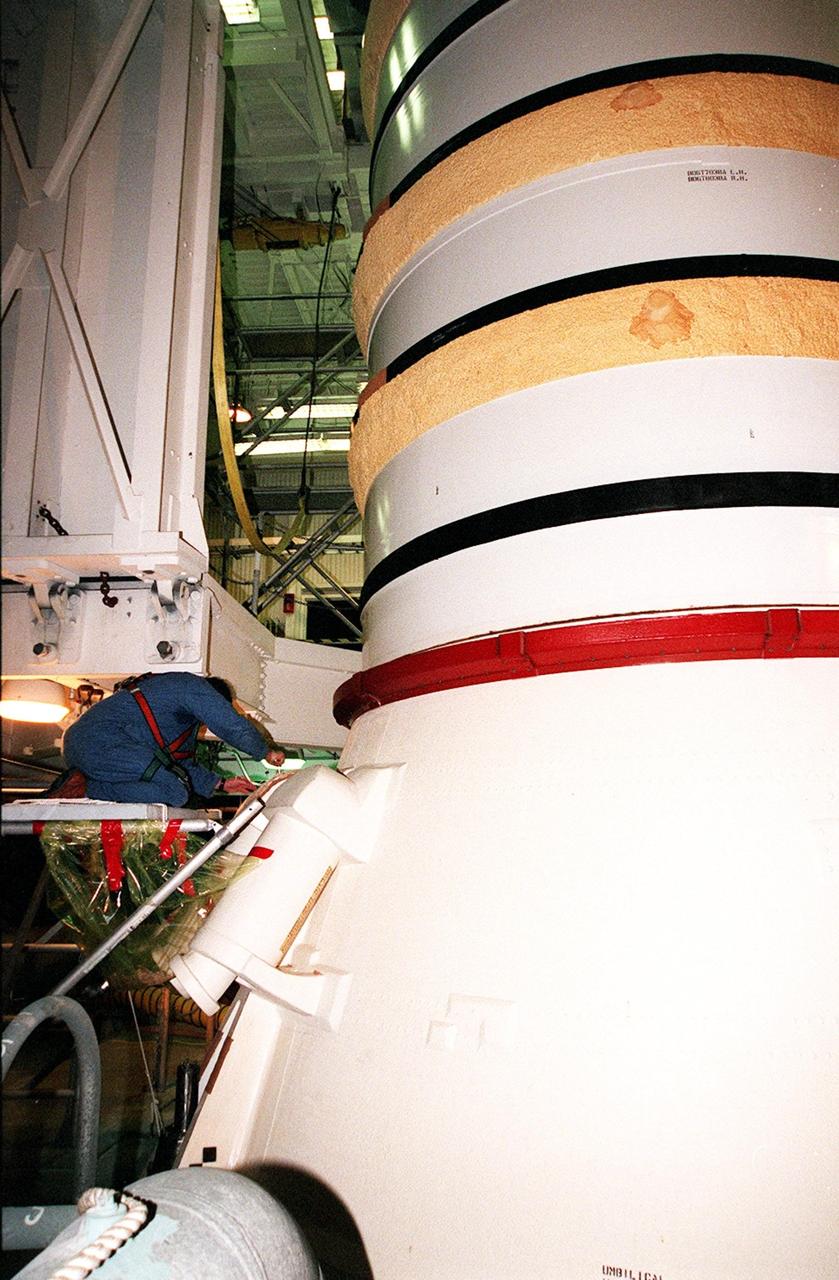 KENNEDY SPACE CENTER, FLA. -- Near the bottom of the solid rocket booster, a worker in the Vehicle Assembly Building begins to detach the SRB system tunnel cover on the 36 cables inside. The SRB is part of Space Shuttle Atlantis, rolled back from Launch Pad 39A in order to conduct tests on the cables. A prior extensive evaluation of NASA’s SRB cable inventory on the shelf revealed conductor damage in four (of about 200) cables. Shuttle managers decided to prove the integrity of the system tunnel cables already on Atlantis before launching. Workers are conducting inspections, making continuity checks and conducting X-ray analysis on the cables. The launch has been rescheduled no earlier than Feb. 6. <br
