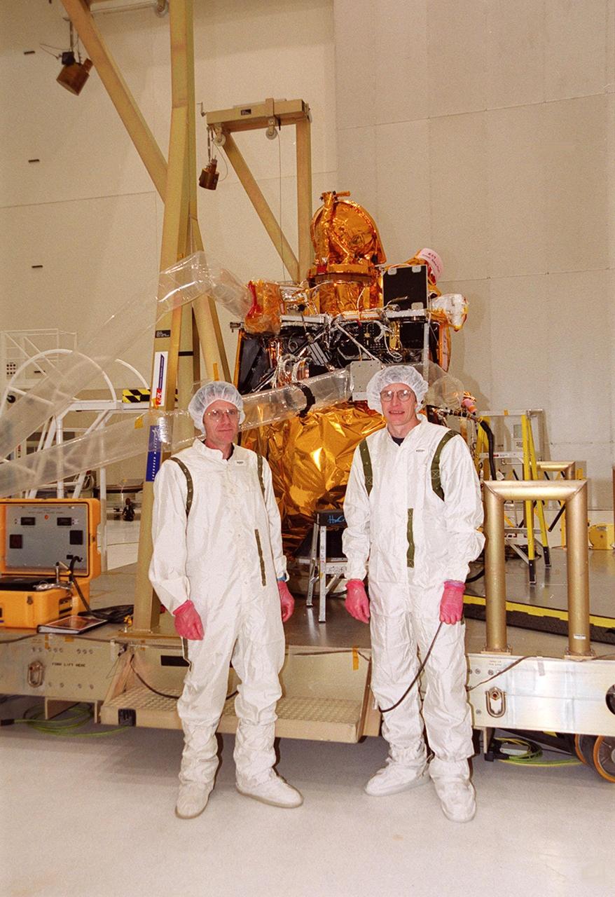 Two technicians involved with the installation of the Gamma Ray Spectrometer (GRS) on the Mars Odyssey Orbiter pose in front of the spacecraft in the Spacecraft Assembly and Encapsulation Facility 2 (SAEF 2).; The orbiter will carry three science instruments: the Thermal Emission Imaging System (THEMIS), the Gamma Ray Spectrometer (GRS), and the Mars Radiation Environment Experiment (MARIE). THEMIS will map the mineralogy and morphology of the Martian surface using a high-resolution camera and a thermal infrared imaging spectrometer. The GRS will achieve global mapping of the elemental composition of the surface and determine the abundance of hydrogen in the shallow subsurface. [The GRS is a rebuild of the instrument lost with the Mars Observer mission.] The MARIE will characterize aspects of the near-space radiation environment with regards to the radiation-related risk to human explorers. The Mars Odyssey Orbiter is scheduled for launch on April 7, 2001, aboard a Delta 7925 rocket from Launch Pad 17-A, Cape Canaveral Air Force Station