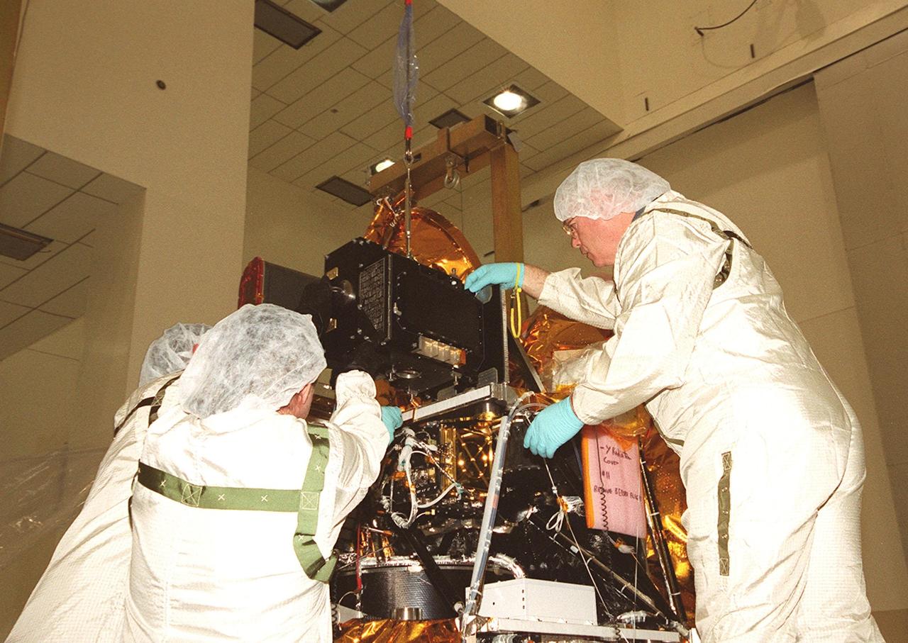 In the Spacecraft Assembly and Encapsulation Facility 2, workers help put the Thermal Emission Imaging System (THEMIS) in its place on the Mars Odyssey Orbiter. THEMIS will map the mineralogy and morphology of the Martian surface using a high-resolution camera and a thermal infrared imaging spectrometer. The orbiter will carry three science instruments: THEMIS, the Gamma Ray Spectrometer (GRS), and the Mars Radiation Environment Experiment (MARIE). The GRS will achieve global mapping of the elemental composition of the surface and determine the abundance of hydrogen in the shallow subsurface. The MARIE will characterize aspects of the near-space radiation environment with regards to the radiation-related risk to human explorers. The Mars Odyssey Orbiter is scheduled for launch on April 7, 2001, aboard a Delta 7925 rocket from Launch Pad 17-A, Cape Canaveral Air Force Station