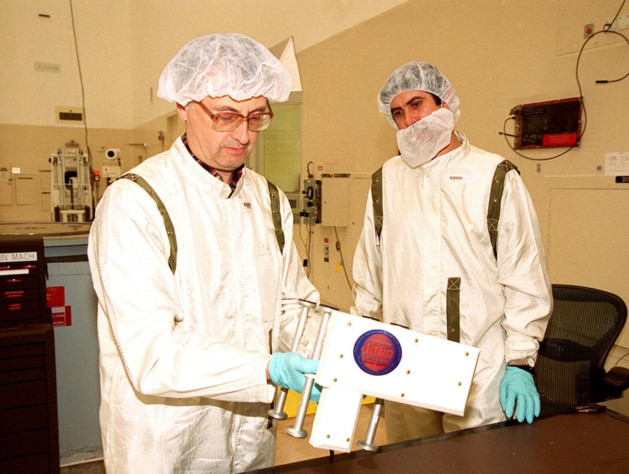 Two Russian scientists look over the High Energy Neutron Detector (HEND), part of the Gamma Ray Spectrometer (GRS), after its removal from the 2001 Mars Odyssey Orbiter. The HEND was built by Russia’s Space Research Institute (IKI). The GRS will achieve global mapping of the elemental composition of the surface and determine the abundance of hydrogen in the shallow subsurface. The orbiter will carry two other science instruments: THEMIS and the Mars Radiation Environment Experiment (MARIE). THEMIS will map the mineralogy and morphology of the Martian surface using a high-resolution camera and a thermal infrared imaging spectrometer. The MARIE will characterize aspects of the near-space radiation environment with regards to the radiation-related risk to human explorers. The Mars Odyssey Orbiter is scheduled for launch April 7, 2001, aboard a Delta 7925 rocket from Launch Pad 17-A, Cape Canaveral Air Force Station