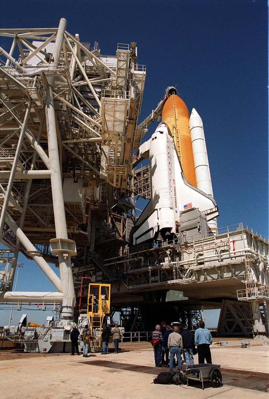 KENNEDY SPACE CENTER, Fla. -- Workers watch the rollback of the Rotating Service Structure (left) from around Space Shuttle Discovery on Launch Pad 39B. Poised above the orange external tank is the Gaseous Oxygen Vent Arm with the “beanie cap,” a vent hood. The RSS provides protected access to the orbiter for changeout and servicing of payloads. It is supported by a rotating bridge that pivots about a vertical axis on the west side of the pad’s flame trench. Space Shuttle Discovery is scheduled to launch March 8 at 6:42 a.m. EST on the eighth construction flight to the International Space Station. It carries the Multi-Purpose Logistics Module Leonardo, the primary delivery system used to resupply and return Station cargo requiring a pressurized environment. Leonardo will deliver up to 10 tons of laboratory racks filled with equipment, experiments and supplies for outfitting the newly installed U.S. Laboratory Destiny