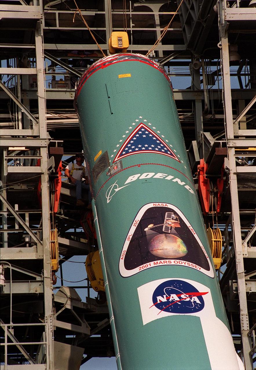The first stage of a Boeing Delta rocket is lifted into place in the gantry on Launch Pad 17-A, Cape Canaveral Air Force Station. The rocket will carry the 2001 Mars Odyssey Orbiter, scheduled for launch April 7, 2001. Mars Odyssey contains three science instruments: THEMIS, the Gamma Ray Spectrometer (GRS), and the Mars Radiation Environment Experiment (MARIE). THEMIS will map the mineralogy and morphology of the Martian surface using a high-resolution camera and a thermal infrared imaging spectrometer. The GRS will achieve global mapping of the elemental composition of the surface and determine the abundance of hydrogen in the shallow subsurface. The MARIE will characterize aspects of the near-space radiation environment with regards to the radiation-related risk to human explorers