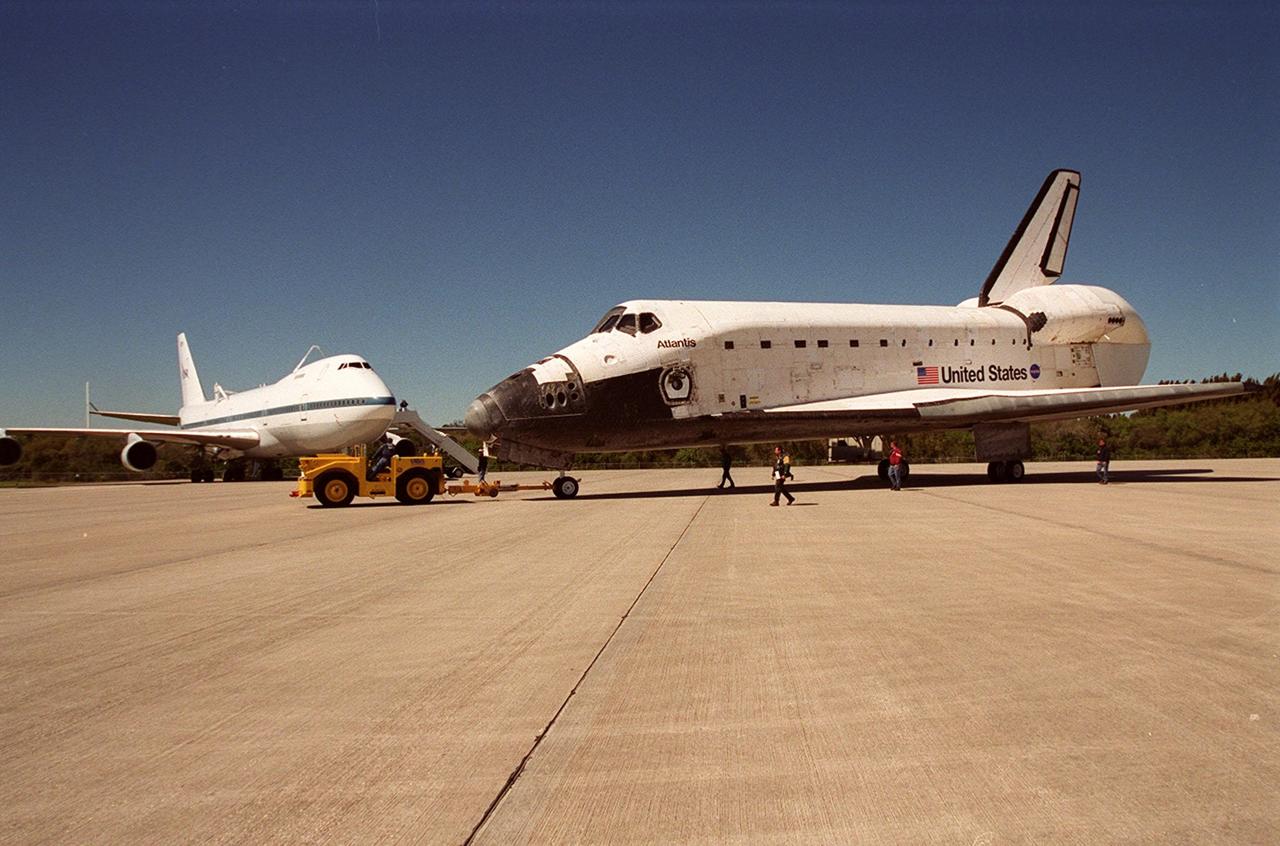 Atlantis is towed from KSC’s Shuttle Landing Facility to the Orbiter Processing Facility. Atlantis returned from California atop a Shuttle Carrier Aircraft (seen in the background, left) after its Feb. 19 landing at Edwards Air Force Base, concluding mission STS-98. The ferry flight began March 1; unfavorable weather conditions kept it on the ground at Altus AFB, Okla., until it could return to Florida. In the Orbiter Processing Facility, Atlantis will be prepared for mission STS-104, the 10th construction flight to the International Space Station, scheduled to launch June 8