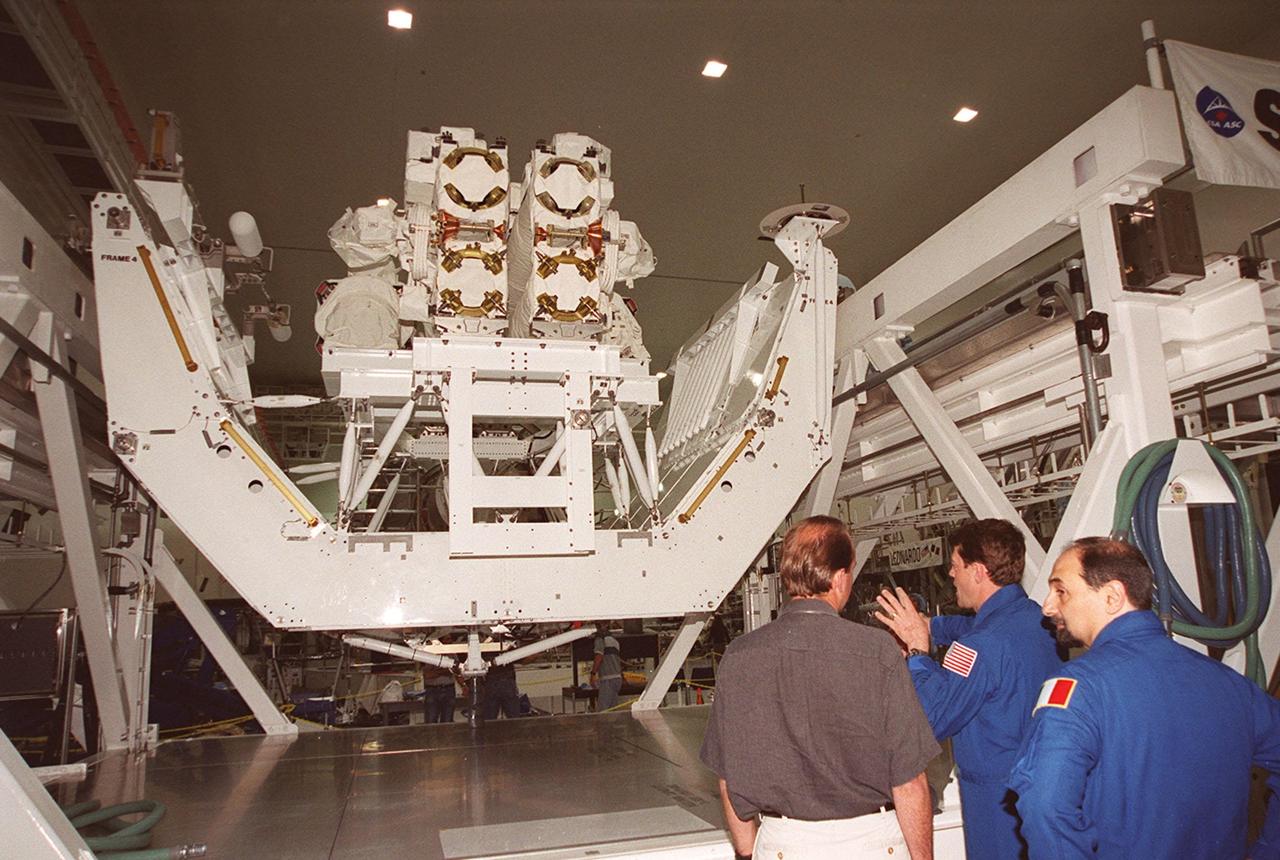 KSC’s PAO videographer, Glenn Benson (left) listens to STS-100 Pilot Jeffrey S. Ashby explain use of the Canadian robotic arm, SSRMS (left), in the Space Station Processing Facility. At right is Mission Specialist Umberto Guidoni. The STS-100 crew is at KSC for Terminal Countdown Demonstration Test activities that include emergency escape training at the pad and a simulated launch countdown. The mission is carrying the Multi-Purpose Logistics Module Raffaello and the SSRMS, to the International Space Station. Raffaello carries six system racks and two storage racks for the U.S. Lab. The SSRMS is crucial to the continued assembly of the orbiting complex. Launch of mission STS-100 is scheduled for April 19 at 2:41 p.m. EDT from Launch Pad 39A