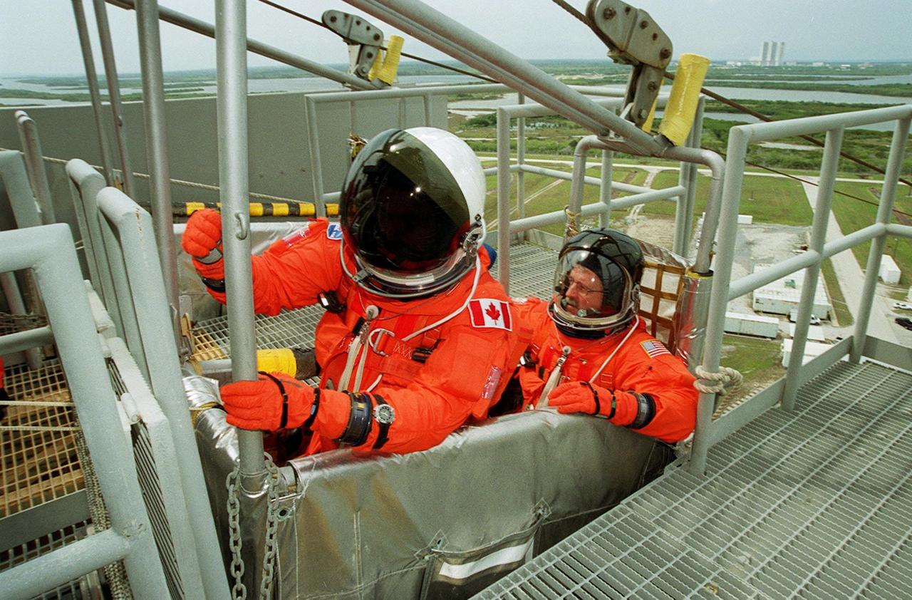 KENNEDY SPACE CENTER, FLA. -- STS-100 Mission Specialists Chris A. Hadfield (left) and John L. Phillips (right) settle in the slidewire basket at Launch Pad 39A. The basket is part of the emergency escape equipment on the pad. The crew is taking part in Terminal Countdown Demonstration Test activities that also include a simulated launch countdown. The mission is carrying the Multi-Purpose Logistics Module Raffaello and the SSRMS, to the International Space Station. Raffaello carries six system racks and two storage racks for the U.S. Lab. The SSRMS is crucial to the continued assembly of the orbiting complex. Launch of mission STS-100 is scheduled for April 19 at 2:41 p.m. EDT from Launch Pad 39A