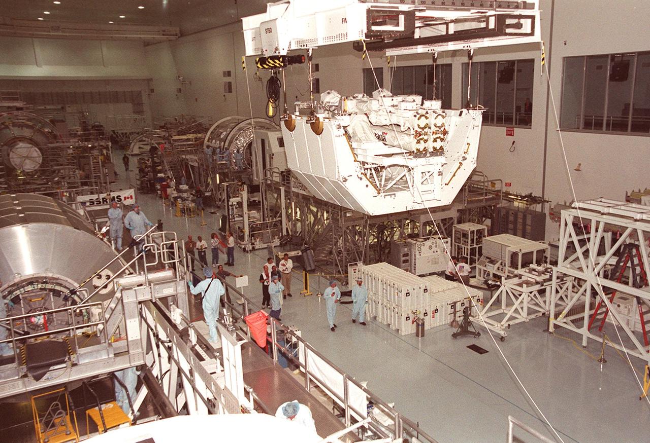 Workers on the floor of the Space Station Processing Facility follow along as the overhead crane carries the Canadian robotic arm, SSRMS, on its pallet to the payload canister. The arm is 57.7 feet (17.6 meters) long when fully extended and has seven motorized joints. It is capable of handling large payloads and assisting with docking the Space Shuttle. The SSRMS is self-relocatable with a Latching End Effector, so it can be attached to complementary ports spread throughout the Station’s exterior surfaces. The SSRMS is part of the payload on mission STS-100, scheduled to launch April 19 at 2:41 p.m. EDT from Launch Pad 39A, KSC