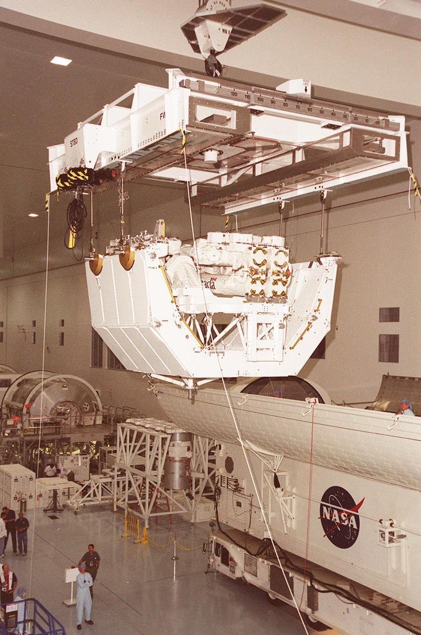 In the Space Station Processing Facility, the overhead crane rolls along the ceiling with the pallet and Canadian robotic arm, SSRMS, toward the payload canister, at right. The arm is 57.7 feet (17.6 meters) long when fully extended and has seven motorized joints. It is capable of handling large payloads and assisting with docking the Space Shuttle. The SSRMS is self-relocatable with a Latching End Effector, so it can be attached to complementary ports spread throughout the Station’s exterior surfaces. The SSRMS is part of the payload on mission STS-100, scheduled to launch April 19 at 2:41 p.m. EDT from Launch Pad 39A, KSC