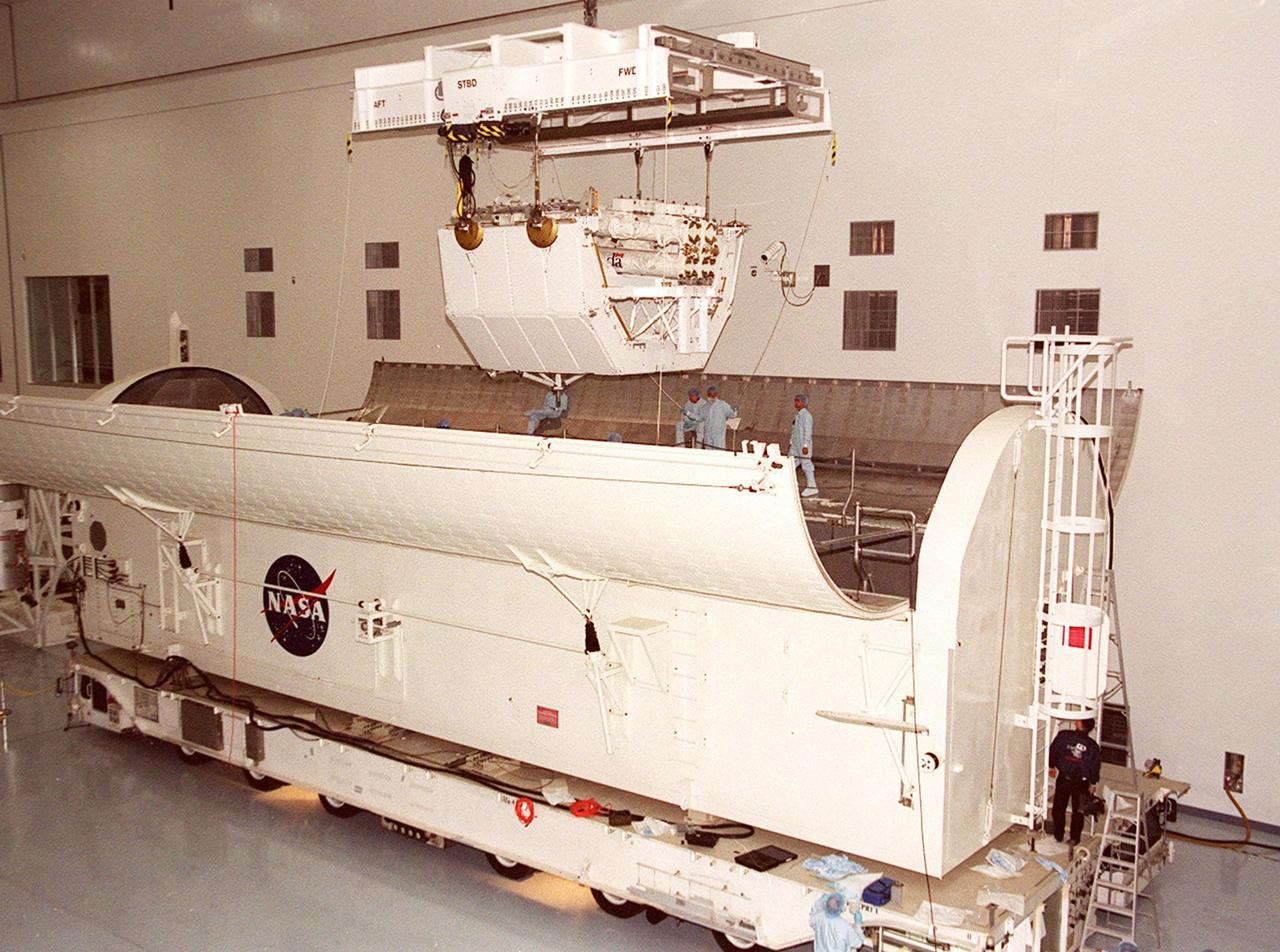 Centered over the payload canister in the Space Station Processing Facility, the overhead crane begins lowering the Canadian robotic arm, SSRMS, on its pallet inside. The arm is 57.7 feet (17.6 meters) long when fully extended and has seven motorized joints. It is capable of handling large payloads and assisting with docking the Space Shuttle. The SSRMS is self-relocatable with a Latching End Effector, so it can be attached to complementary ports spread throughout the Station’s exterior surfaces. The SSRMS is part of the payload on mission STS-100, scheduled to launch April 19 at 2:41 p.m. EDT from Launch Pad 39A, KSC