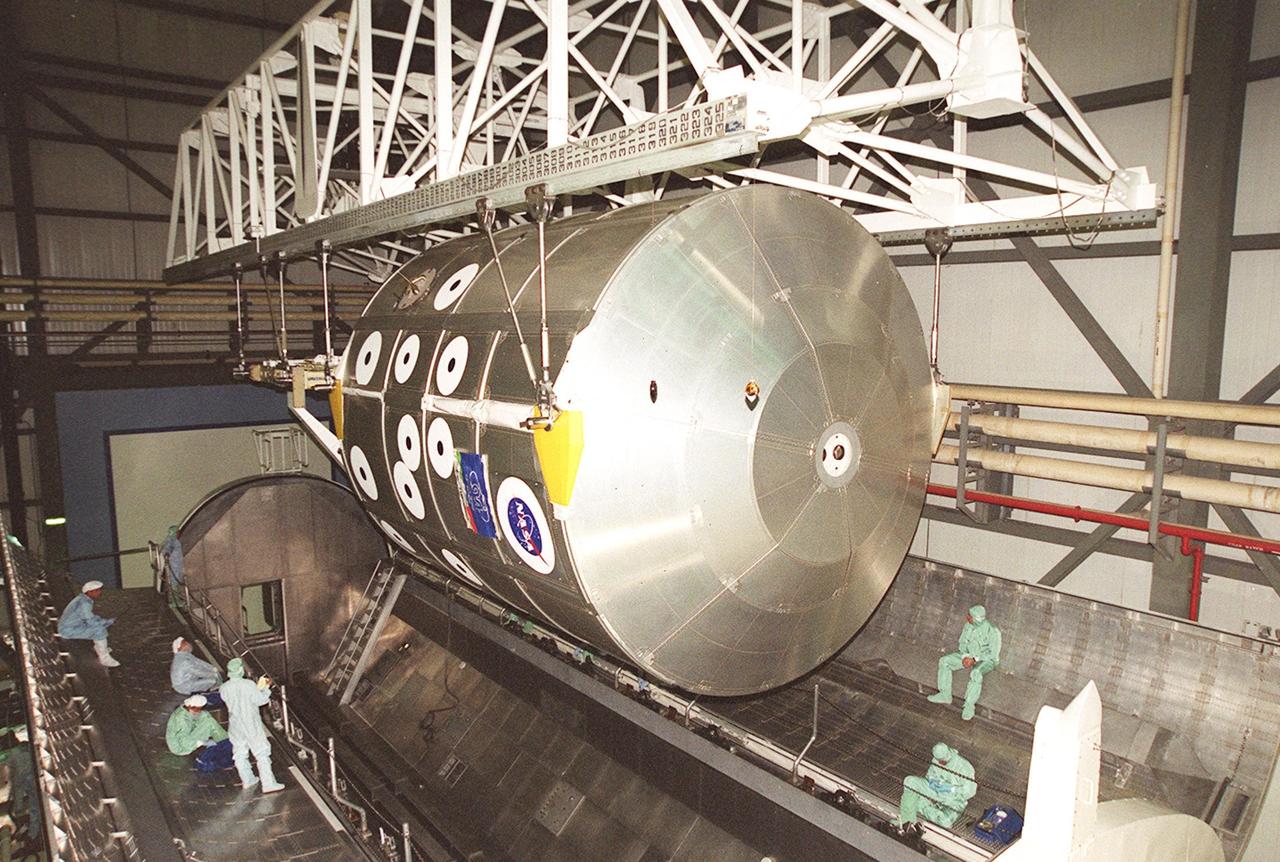 KENNEDY SPACE CENTER, FLA. -- In the Orbiter Processing Facility bay 2, an overhead crane positions the Multi-Purpose Logistics Module Leonardo and the integrated cargo carrier behind it above a payload canister. The MPLM has just returned from its first round trip to the International Space Station on mission STS-102. Leonardo will be transferred to the SSPF to prepare it for future missions. The MPLM serves as a cargo van, carrying equipment and supplies to the Space Station